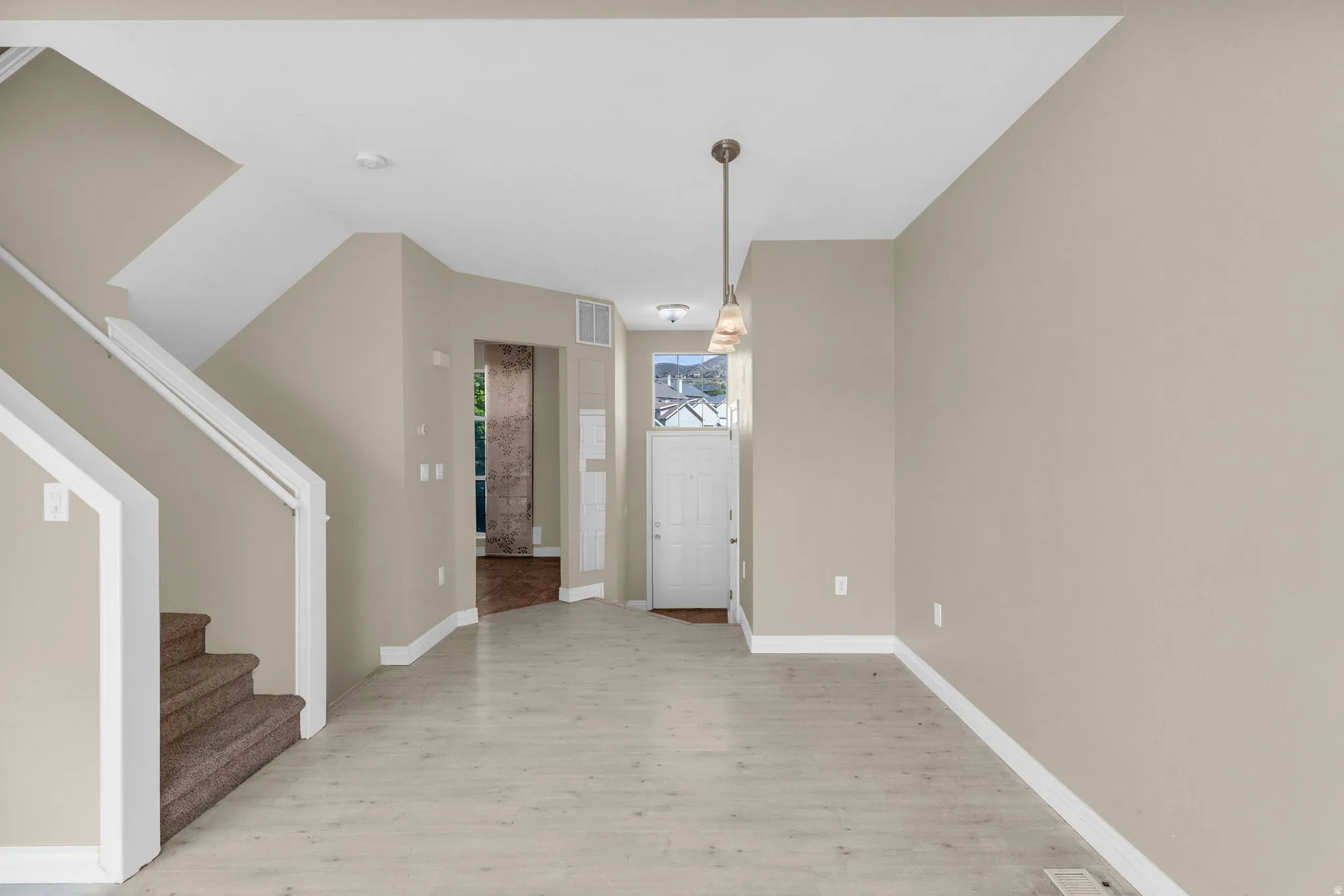 Open-concept area featuring light wood-finish flooring, neutral wall paint, and a modern pendant light fixture