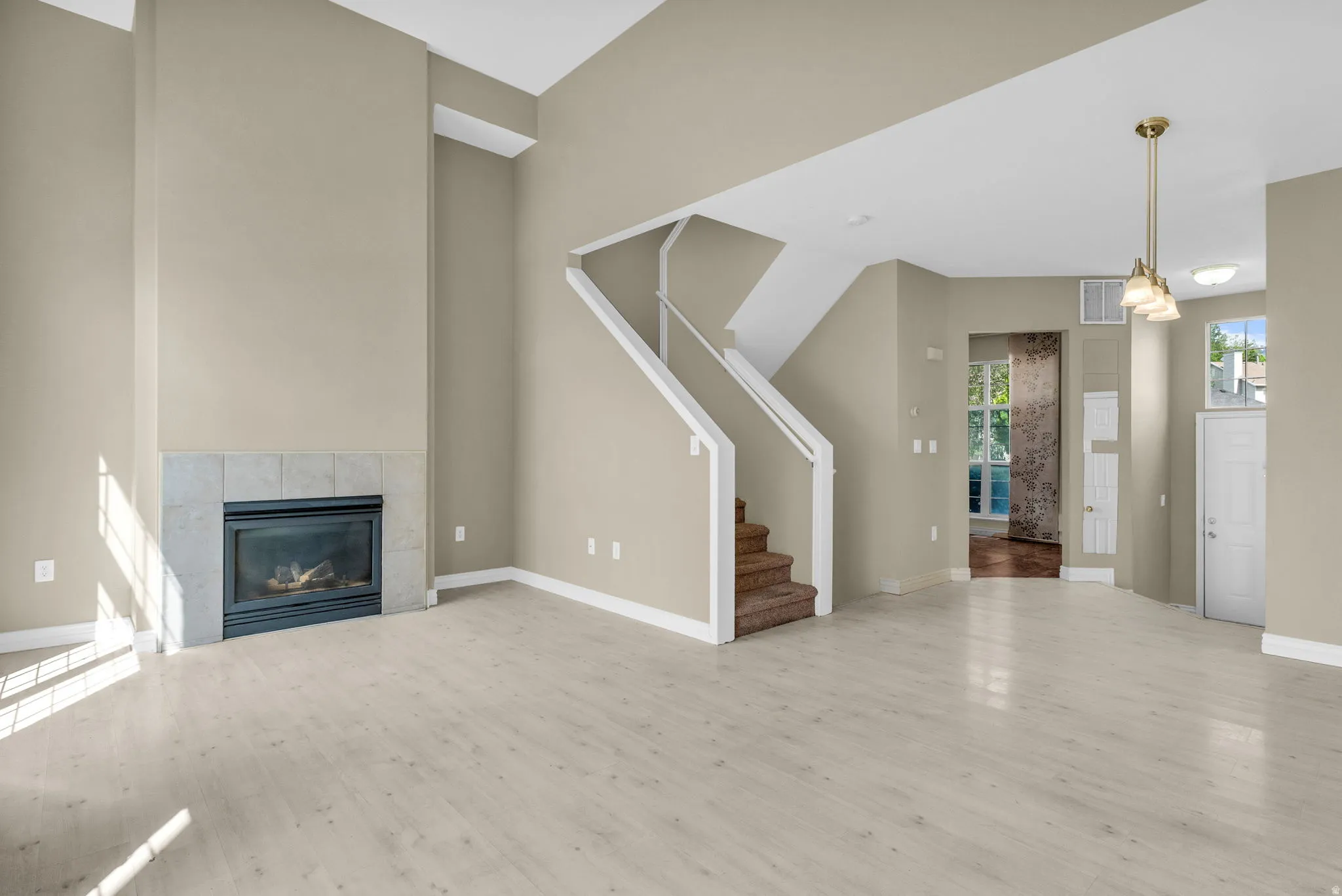 Living area featuring vaulted ceilings, wood-finish flooring, a tile-surround fireplace, and a multi-tiered staircase