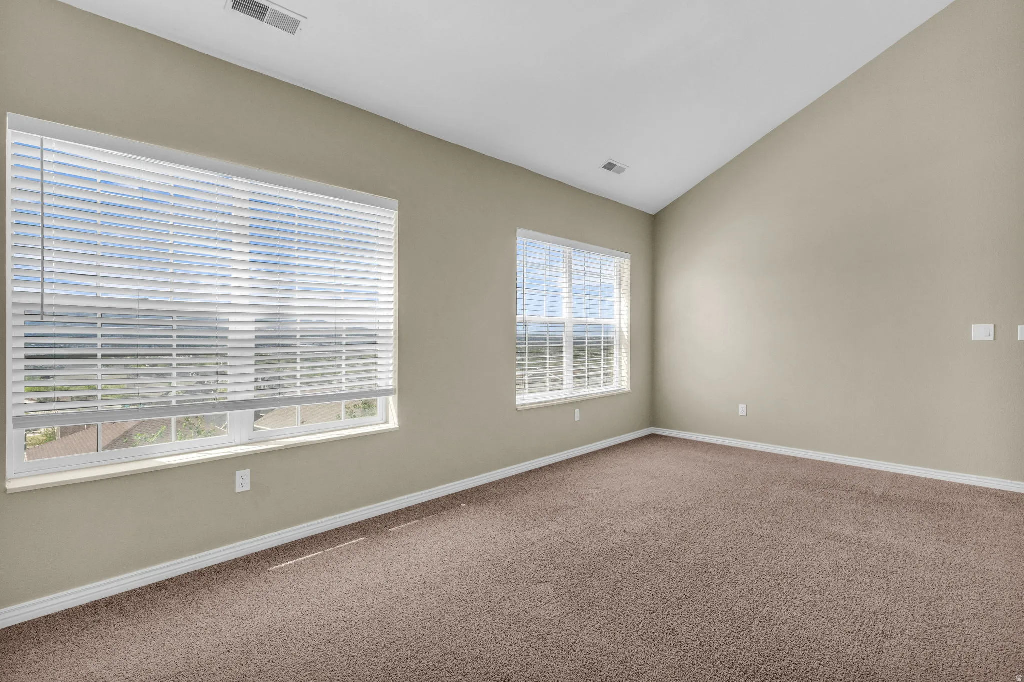 Spacious room featuring vaulted ceilings, light tan walls, and brown carpeting