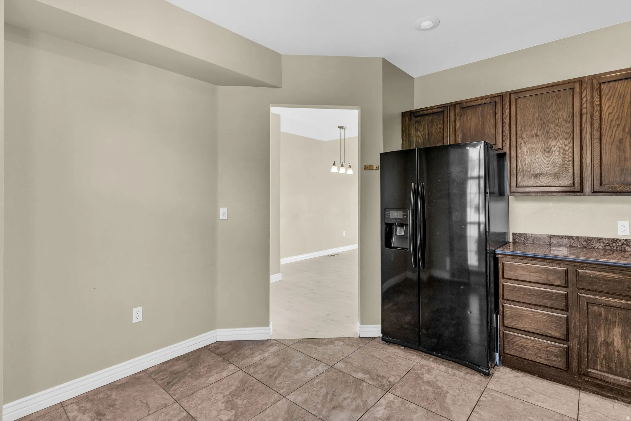 Kitchen area featuring a side-by-side refrigerator, wood-finish cabinetry, and stone-look tile flooring