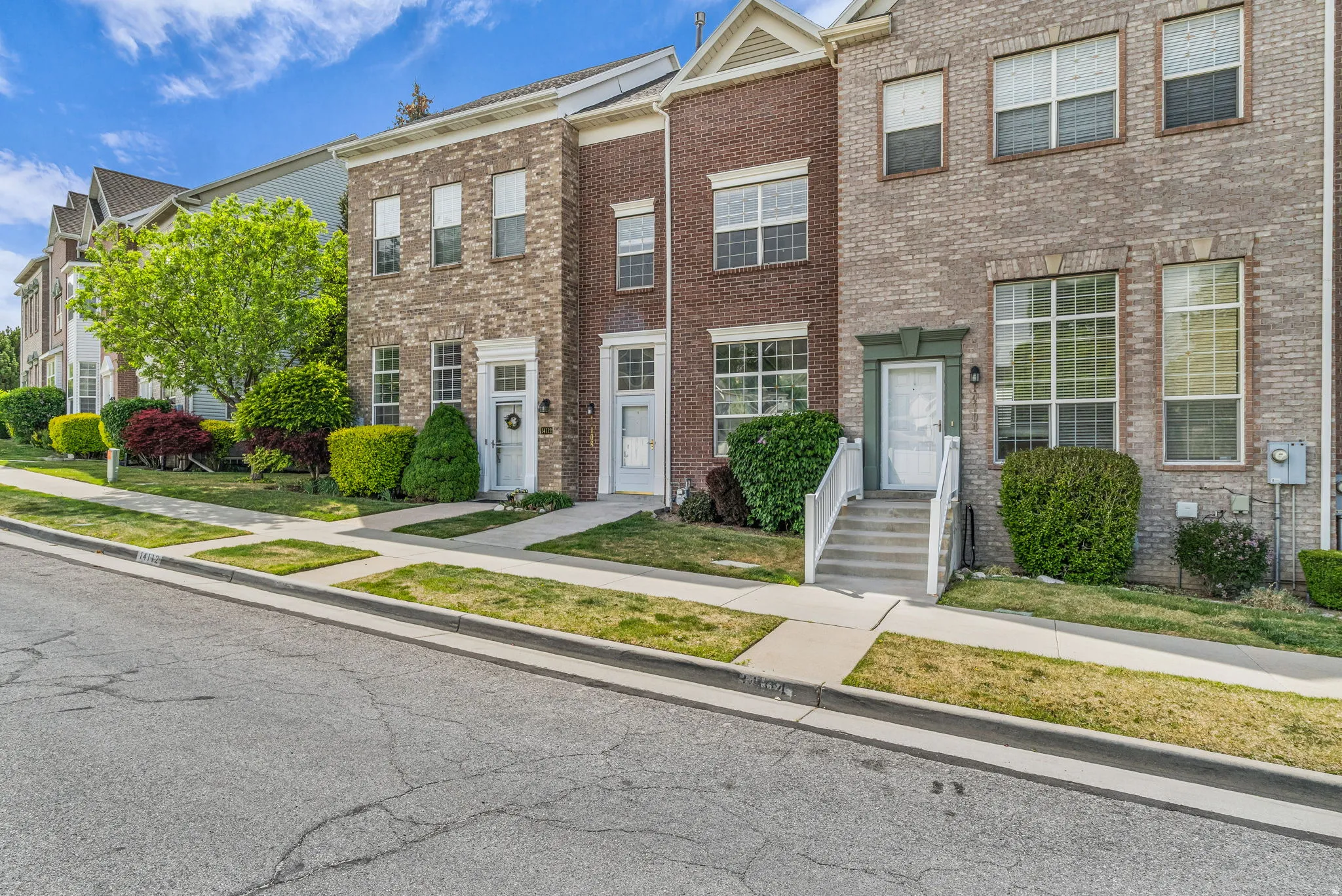 Brick and stone facade townhome featuring multiple large windows, decorative front door surrounds, and manicured landscaping
