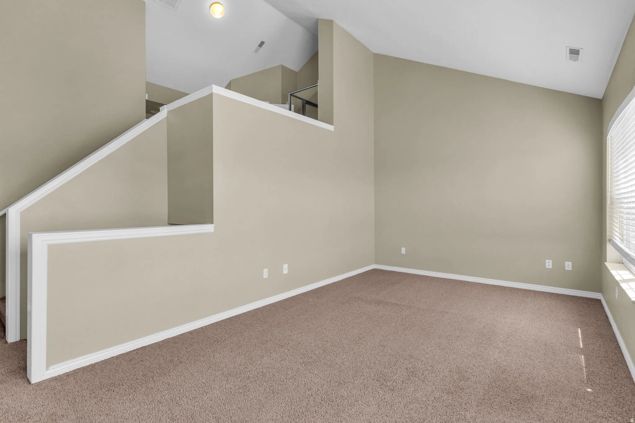Carpeted room featuring a distinctive vaulted ceiling, a staircase with white trim, and a window with horizontal blinds
