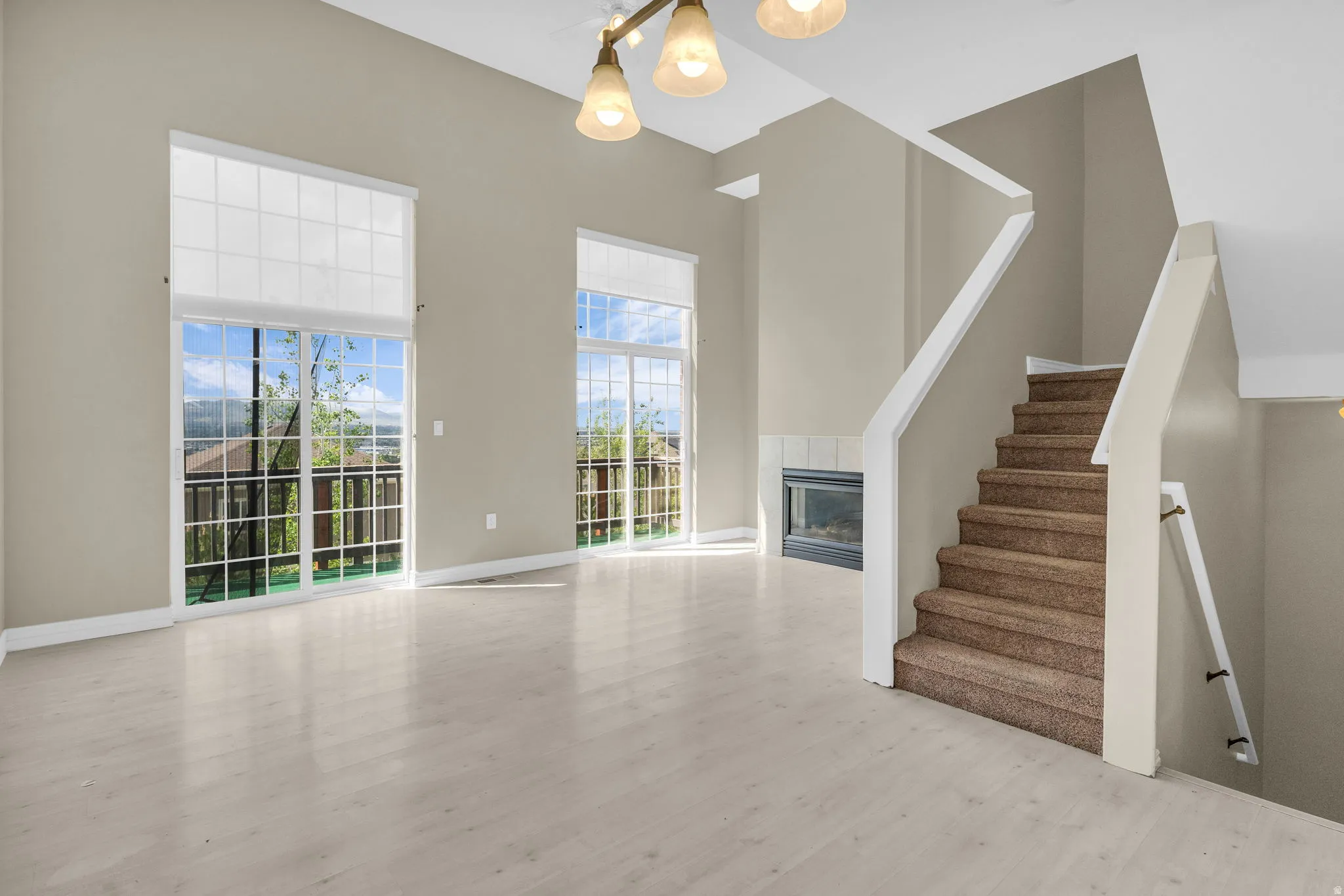Spacious room featuring vaulted ceilings, light wood-finish flooring, two large sliding glass doors with upper windows, and a built-in fireplace with a tiled surround