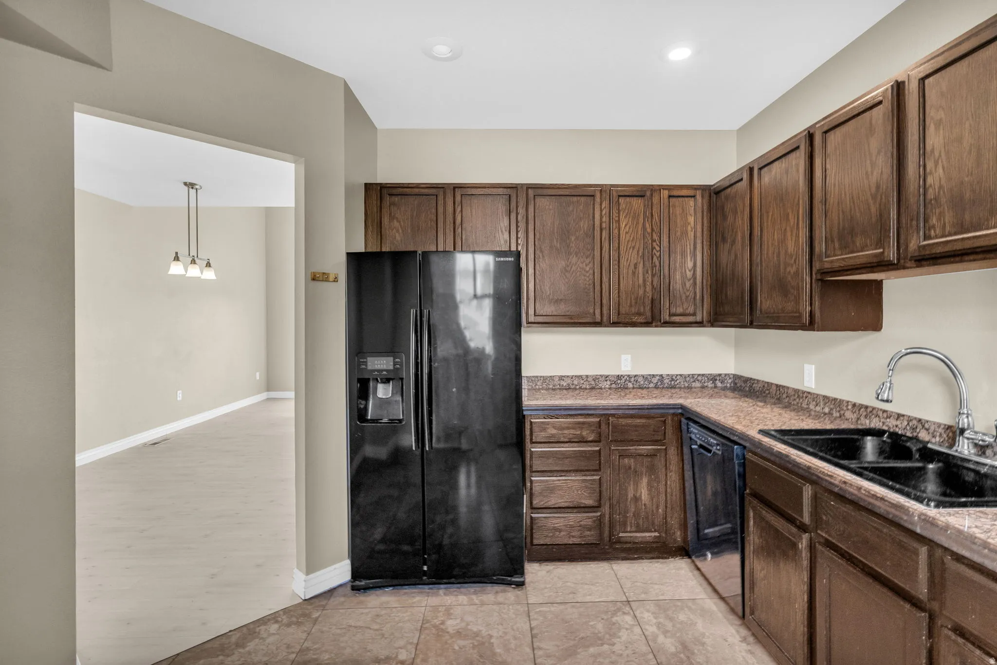 Kitchen featuring wood cabinetry, stone-look countertops, a black side-by-side refrigerator, a black double-basin sink with a chrome faucet, and tile flooring