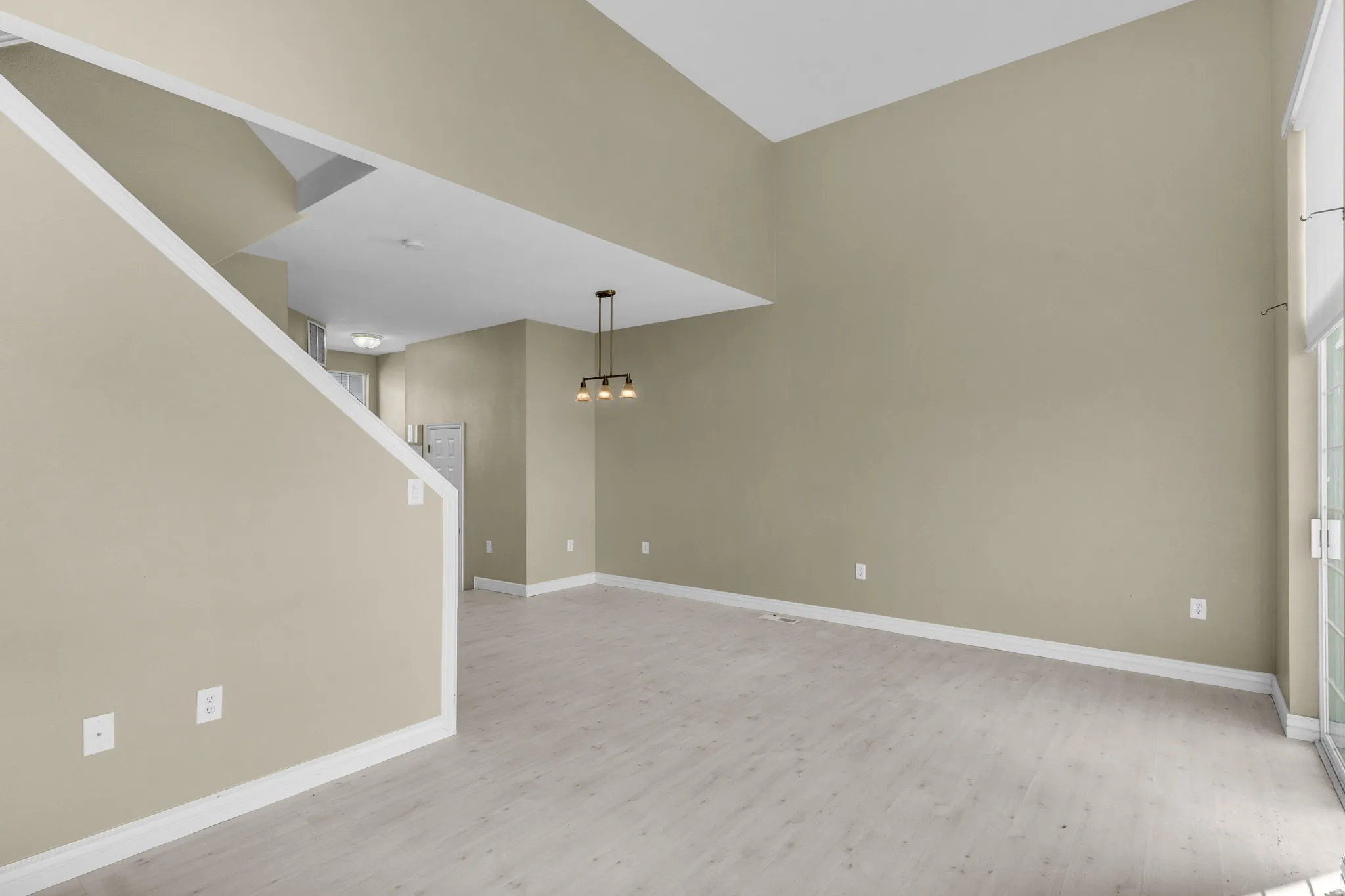 Spacious interior featuring a high vaulted ceiling, light wood-finish flooring, sliding glass patio doors, and an open staircase