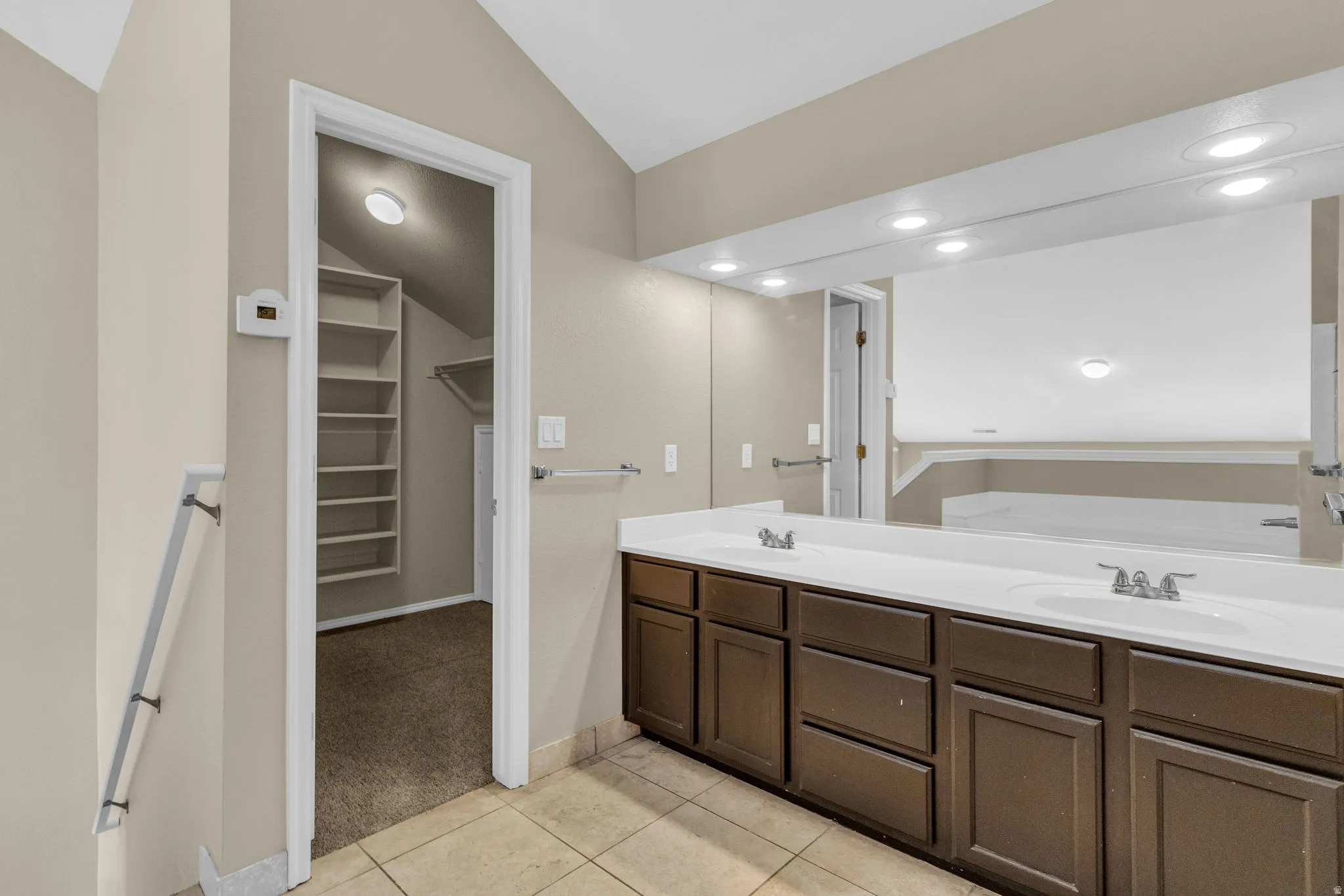 Double vanity with integrated sinks, ample storage cabinetry, and an expansive wall-mounted mirror with recessed lighting