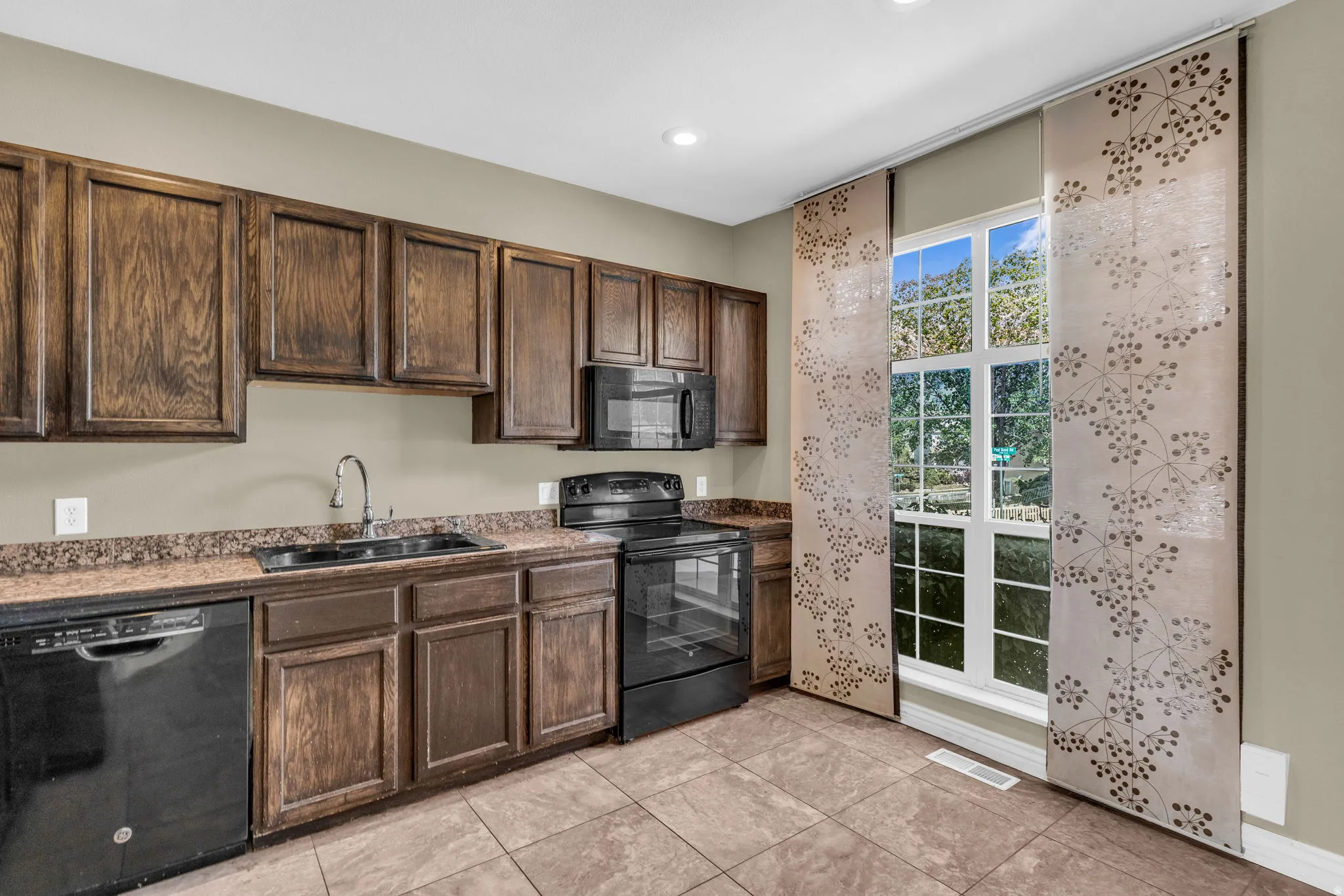 Kitchen area featuring dark wood-finish cabinetry, black appliances including a dishwasher and range, and a dual basin sink with a chrome faucet