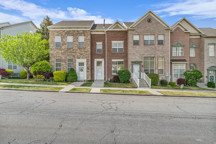 Multi-story brick and stone facade townhome featuring white entry doors, white window frames, and manicured shrubbery