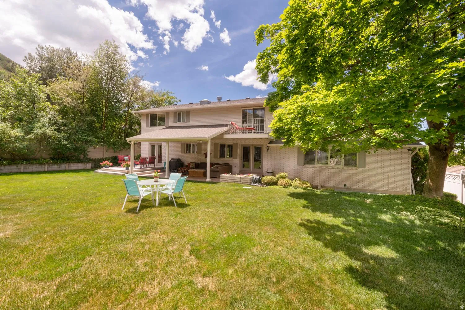 Expansive green lawn extending to a multi-level home with a covered patio, upper-level balcony, and a paved outdoor dining area