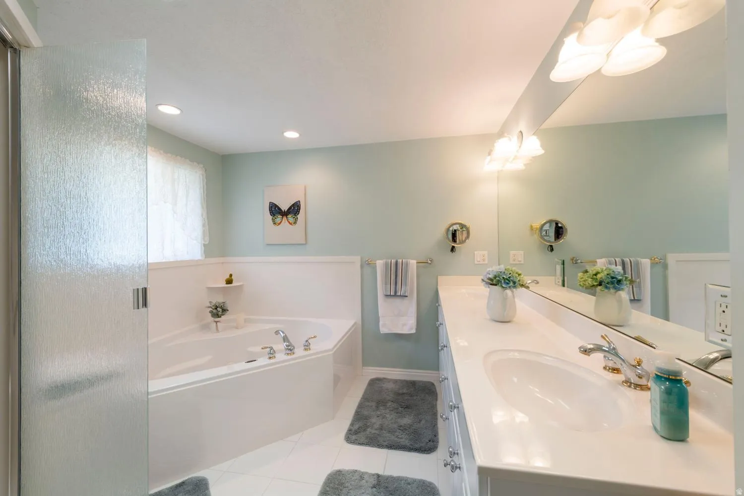 Bathroom featuring a corner soaking tub with deck-mounted fixtures, a vanity with dual sinks and a white countertop, and a large wall-mounted mirror
