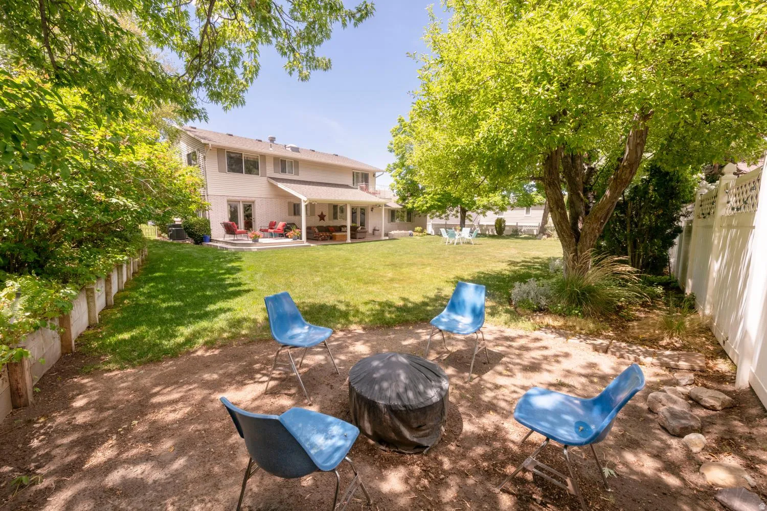 Expansive outdoor area featuring a two-story residence with a covered patio, a manicured lawn, mature trees, and a gravel gathering space