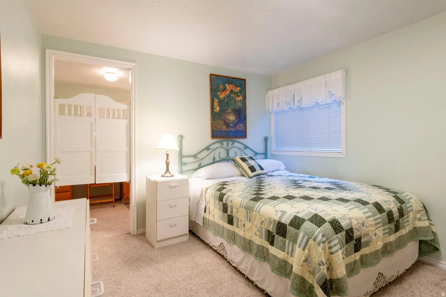 Bedroom with light green walls and white trim, featuring a single window with blinds and valance