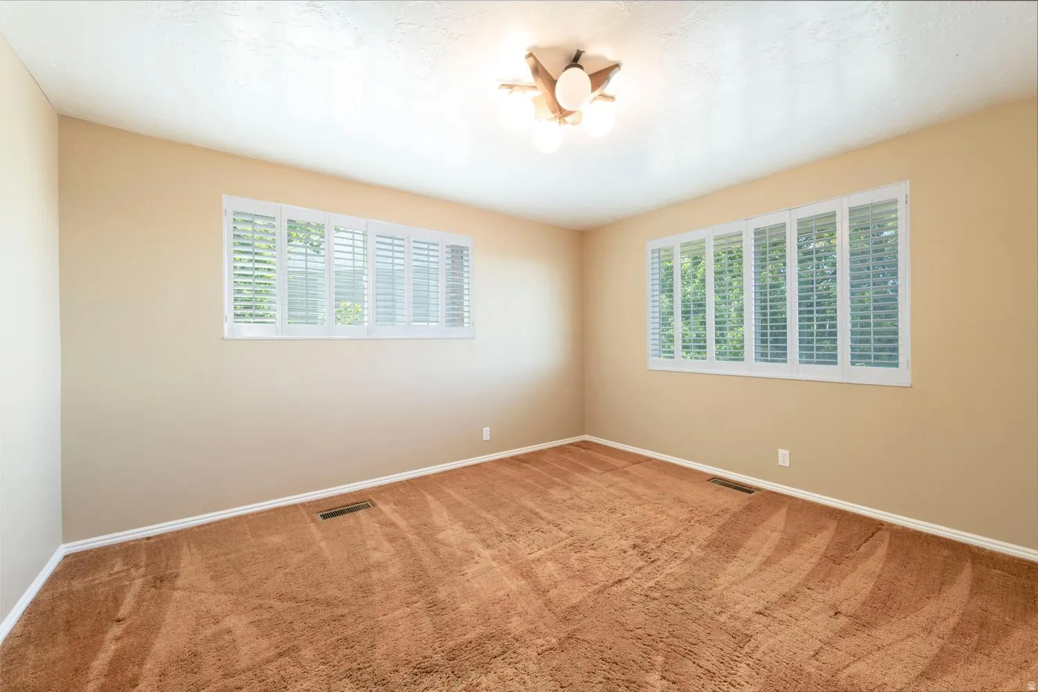 Interior room featuring two large windows with white louvered shutters, neutral-toned walls, brown carpeting, and a ceiling-mounted light fixture