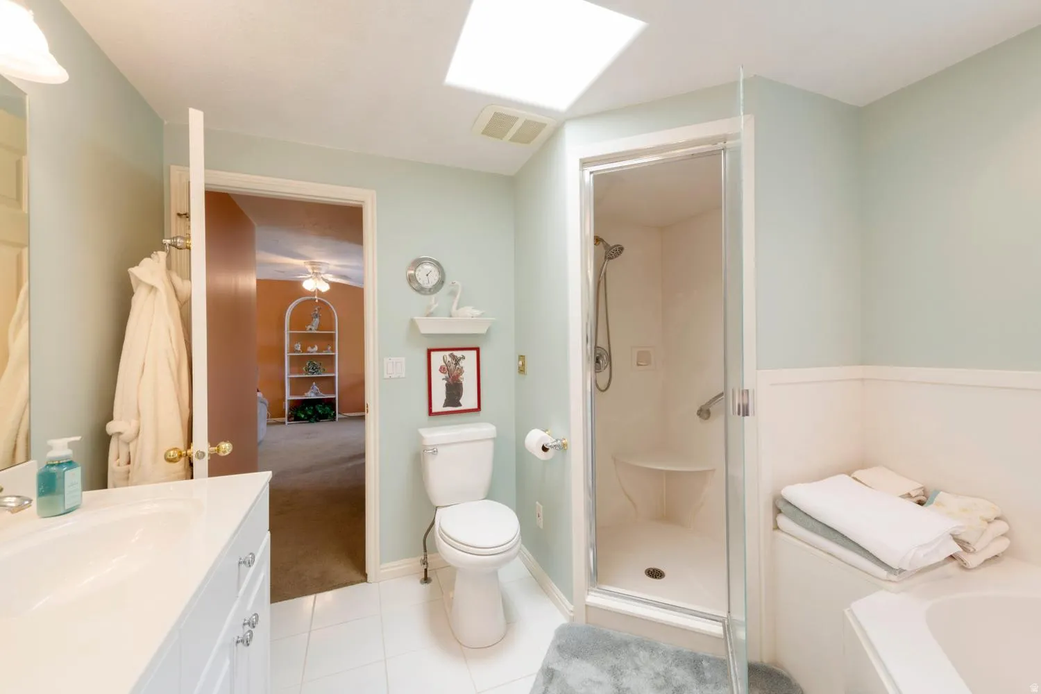 Full bathroom featuring a glass-enclosed shower with built-in seating, a separate soaking tub, a single vanity with storage, and a skylight for natural illumination