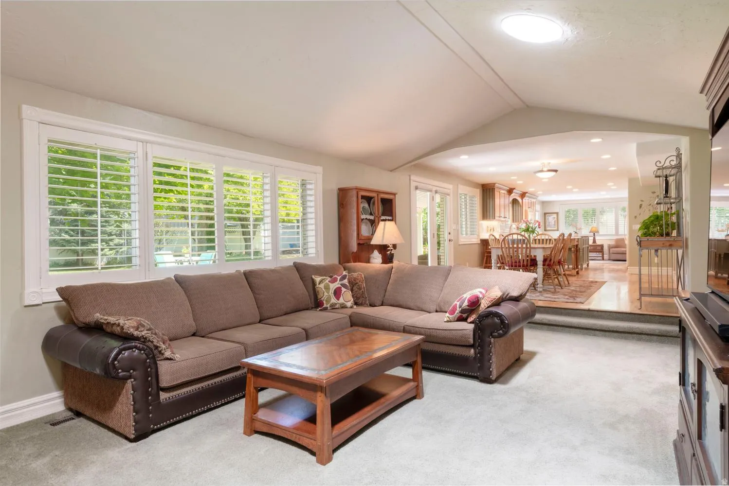 Spacious living area featuring a large window array with plantation shutters, a vaulted ceiling, and a skylight