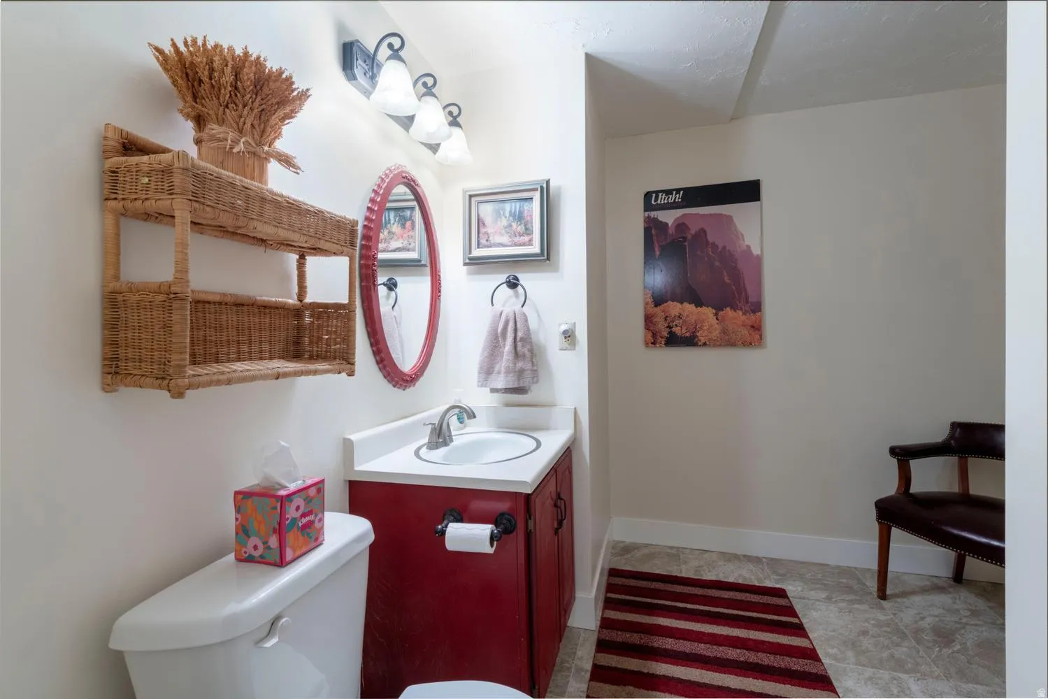 Bathroom featuring a white toilet, red-painted vanity with a white countertop and integrated sink, a wall-mounted mirror with a red frame, and an overhead vanity light fixture