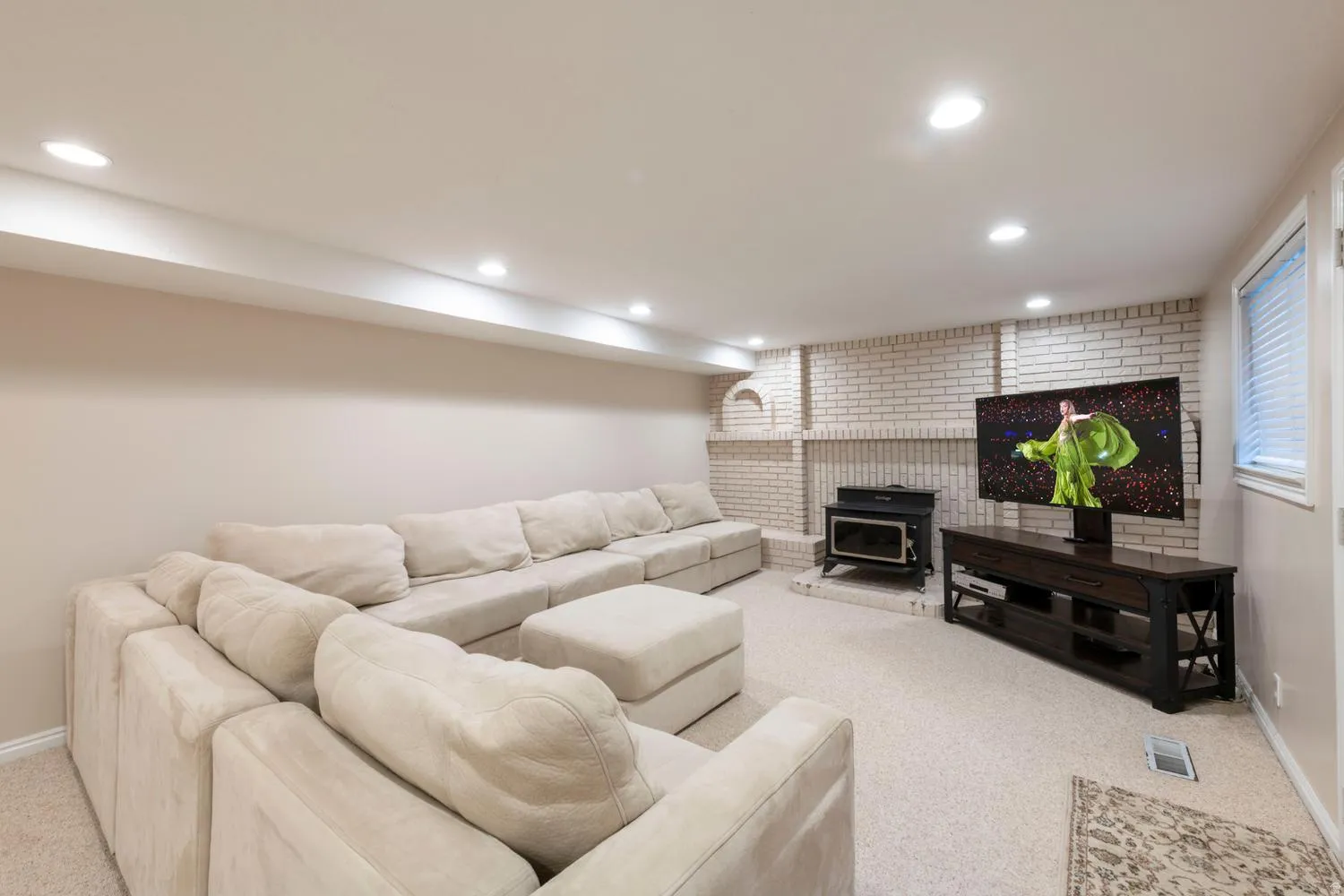 Carpeted recreation room featuring recessed lighting, a painted brick accent wall, and a built-in wood stove