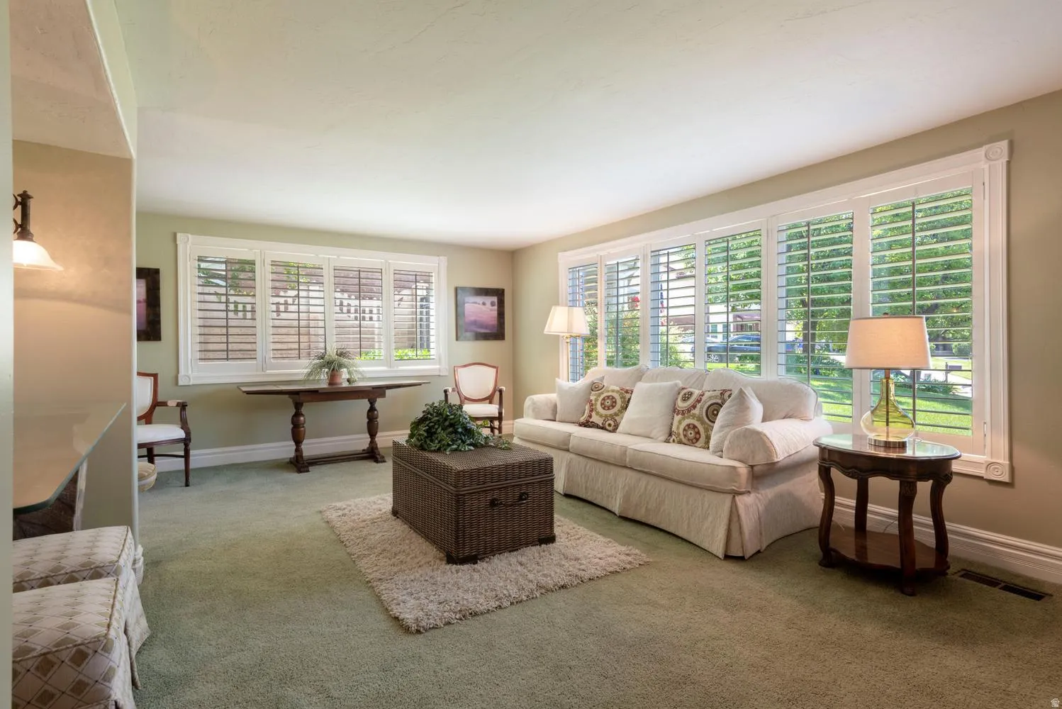 Living room featuring a large picture window with plantation shutters, additional window with plantation shutters, and a wall sconce