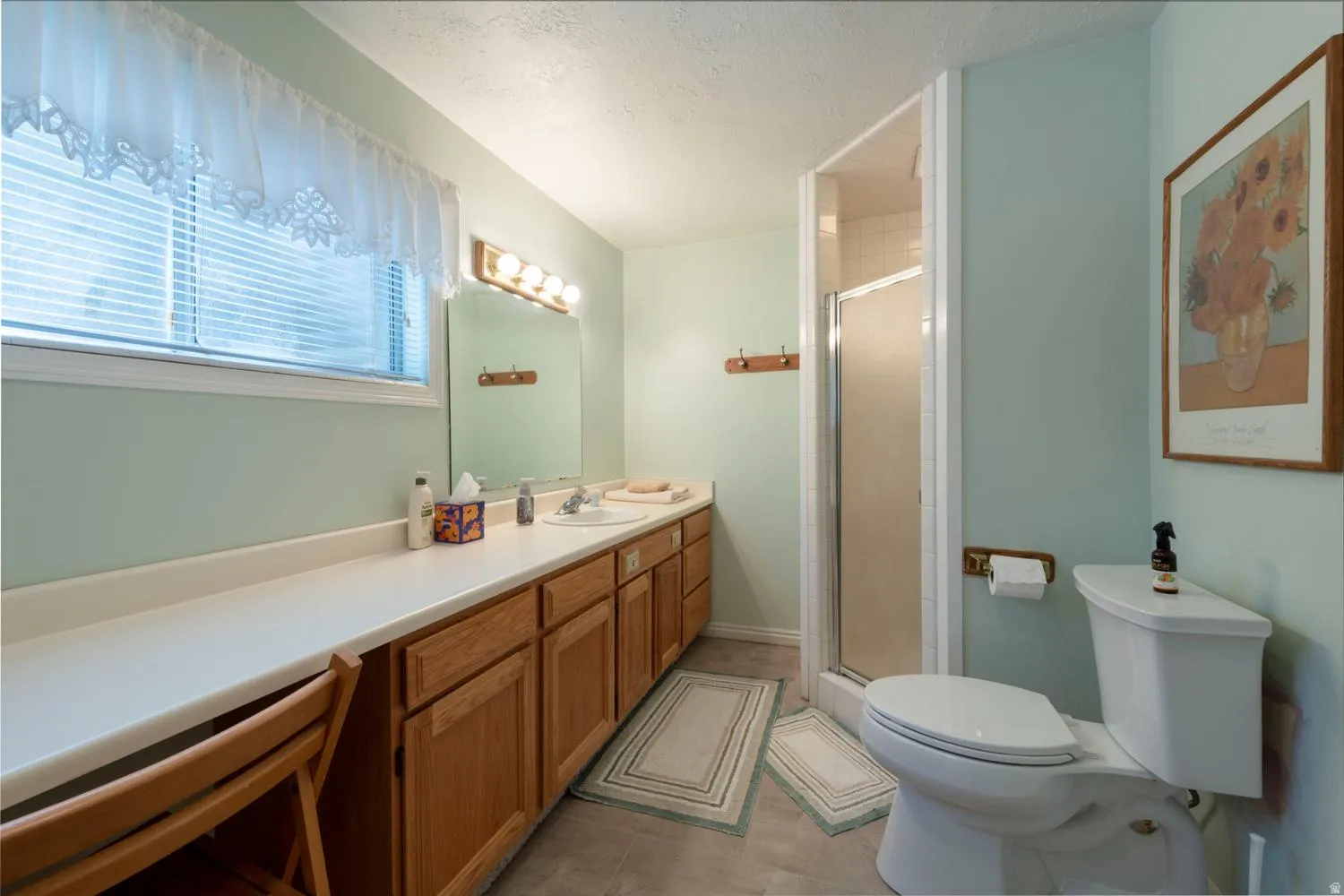 Bathroom featuring a double vanity with light wood cabinetry, a built-in shower stall, and a window with horizontal blinds