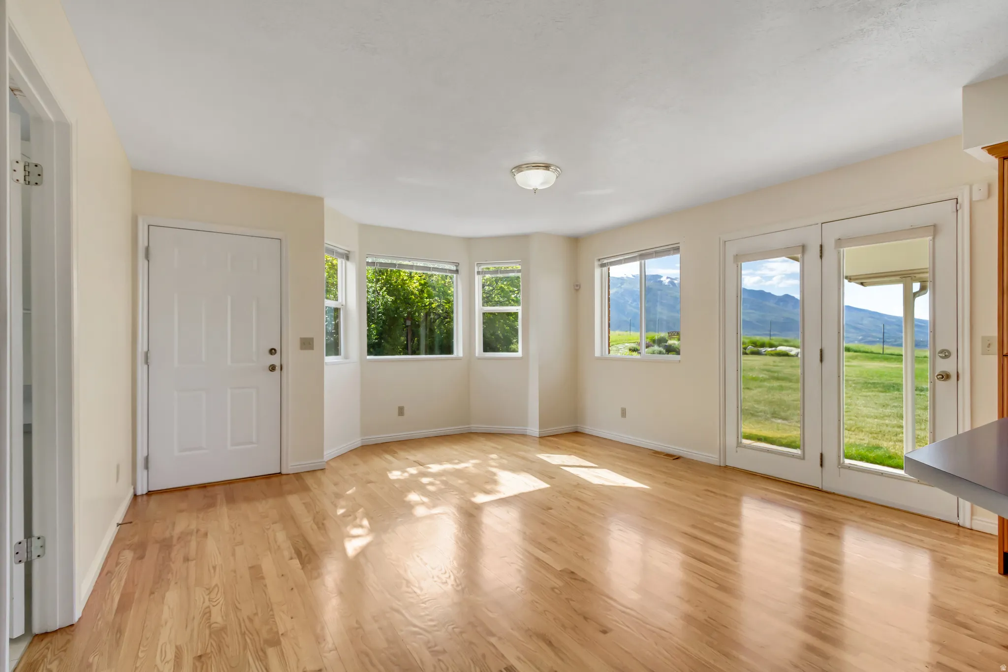 Expansive room featuring wood-finish flooring, white trim, multiple windows, and exterior access via double French doors