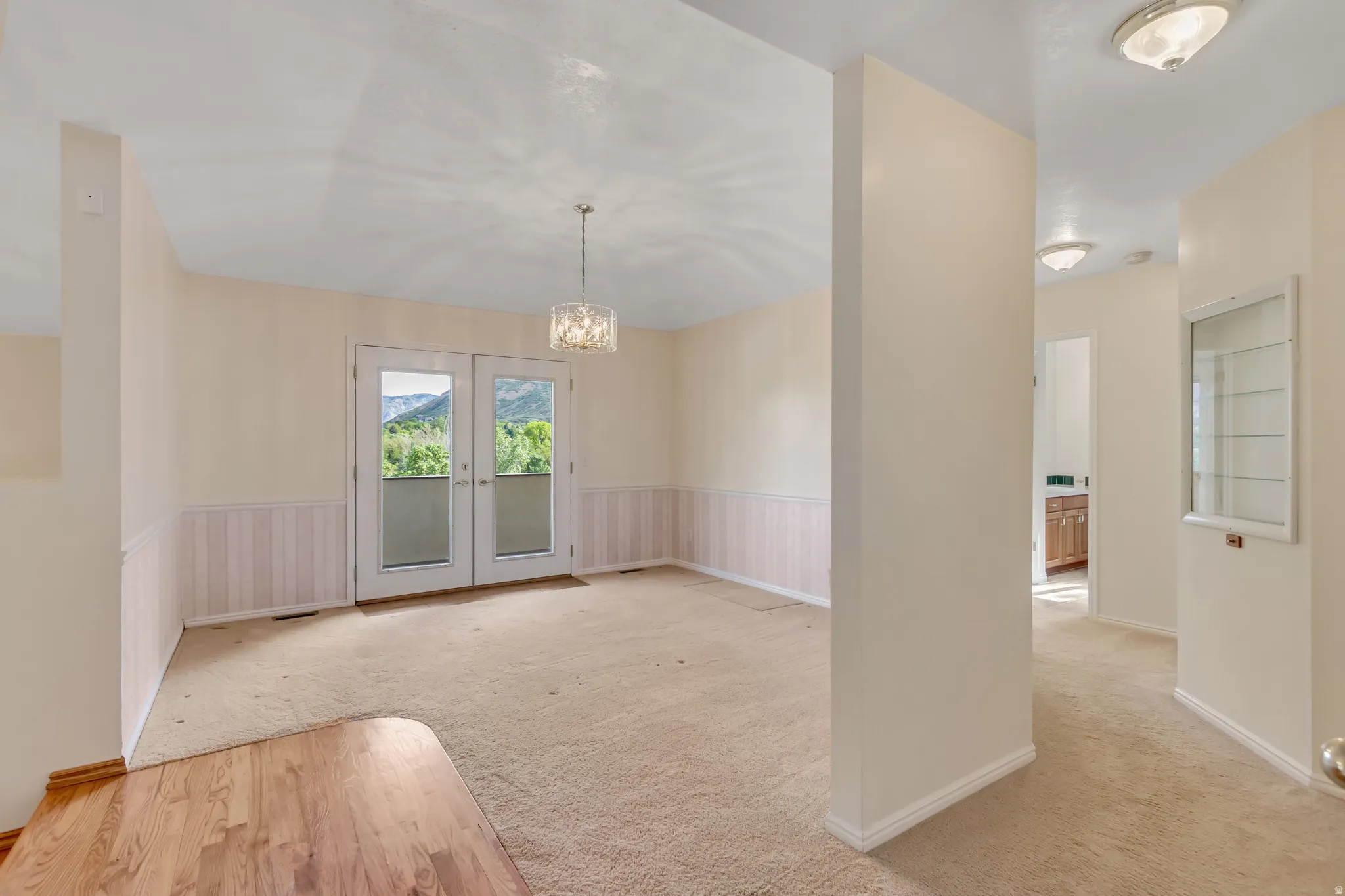 Interior space with French doors, a crystal chandelier, half-wall wainscoting, and a combination of carpet and wood-finish flooring