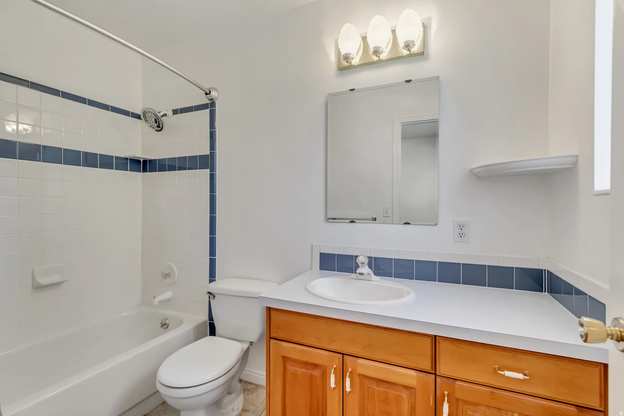 Bathroom featuring a white bathtub and shower with blue accent tiling, a toilet, and a vanity with wood cabinetry, a white countertop, and an integrated sink