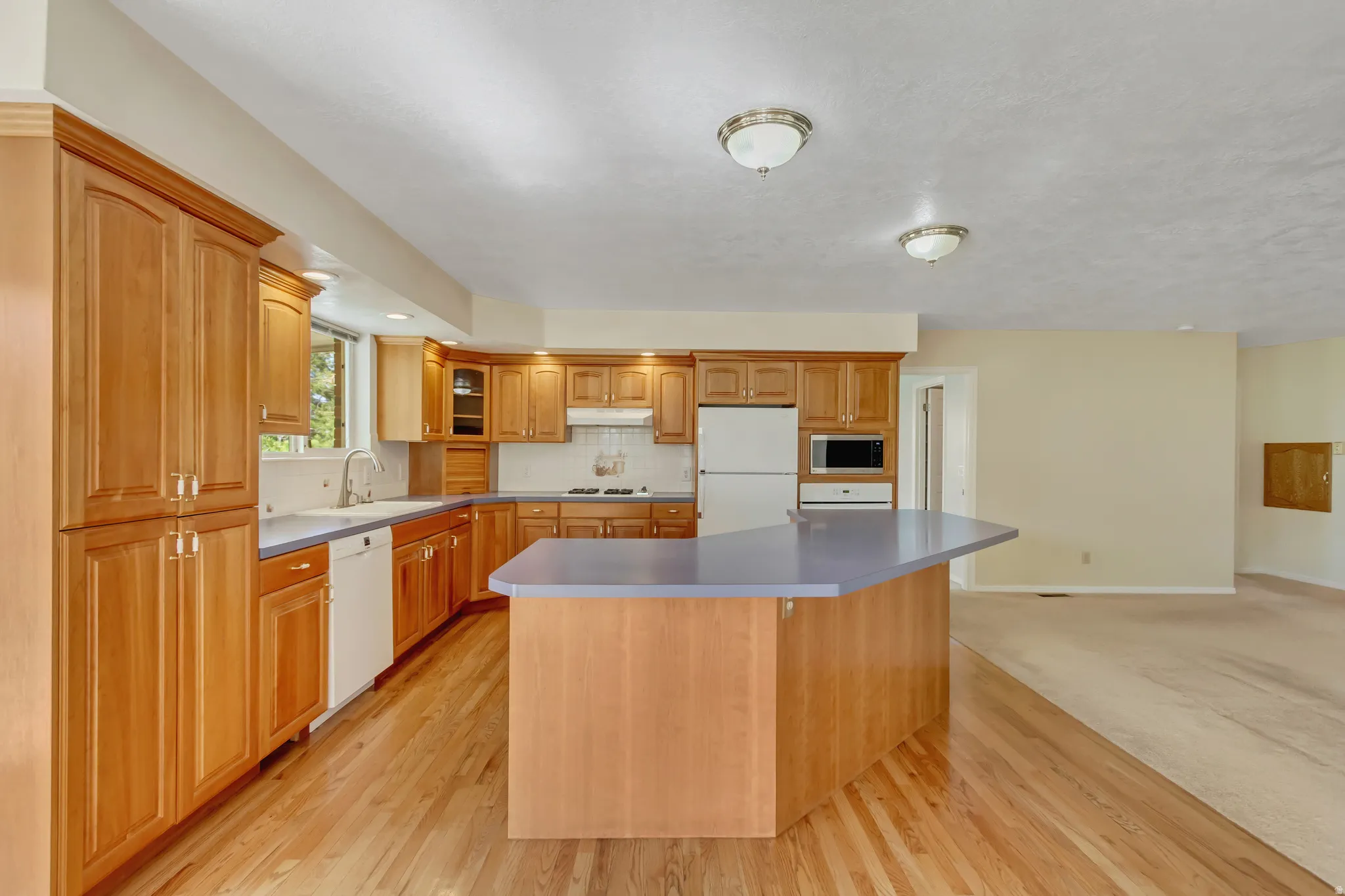 Open-concept kitchen featuring wood cabinetry, wood-finish flooring, a central island with a contrasting countertop, and integrated appliances