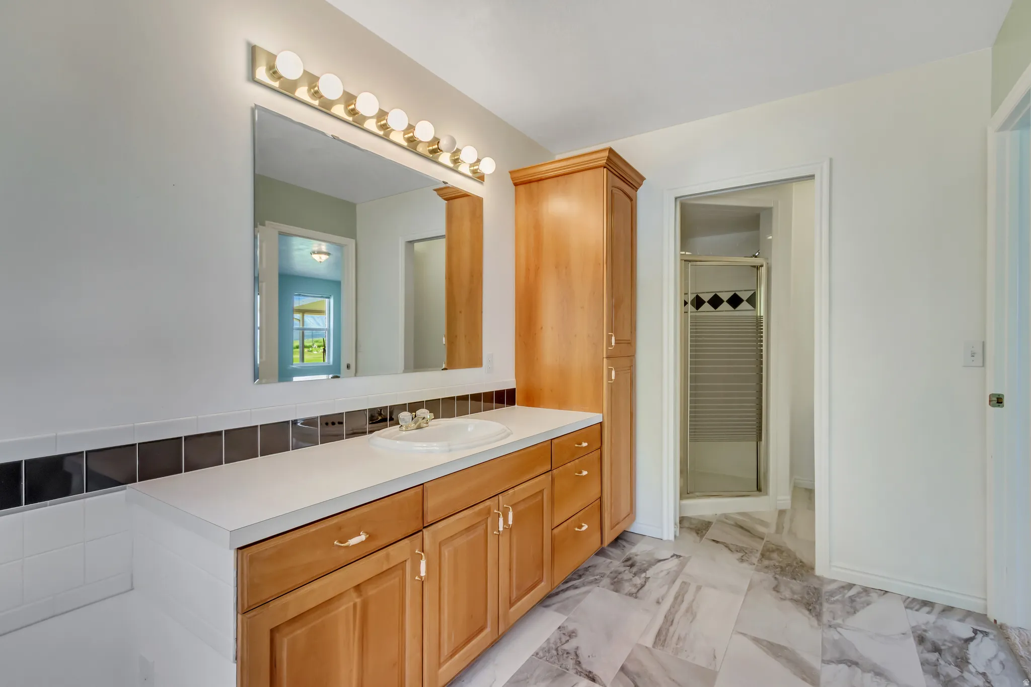 Bathroom featuring a single vanity with light wood cabinetry, a white countertop, and an integrated sink