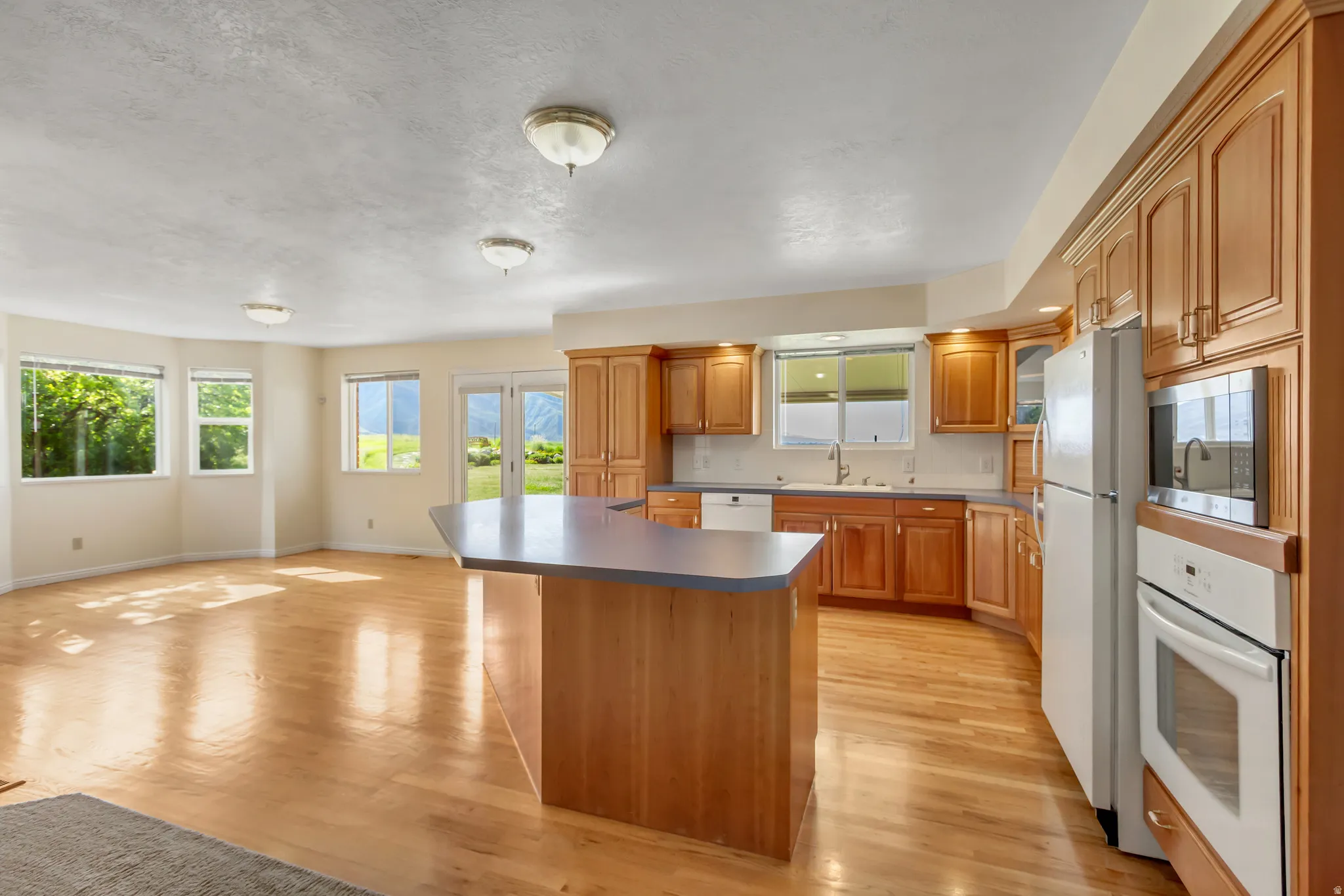 Spacious kitchen with a central island featuring a gray countertop, extensive wood cabinetry, and a full suite of built-in appliances including a wall oven and microwave