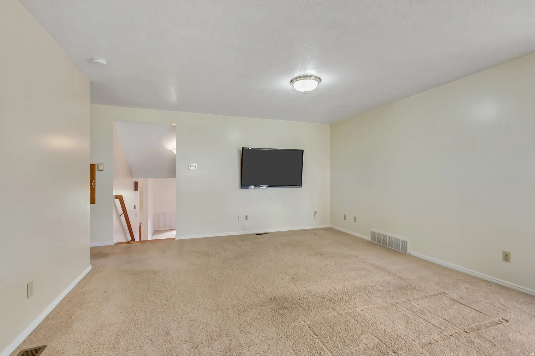 Carpeted living area featuring light-toned walls, a flush-mount ceiling light, and baseboard trim