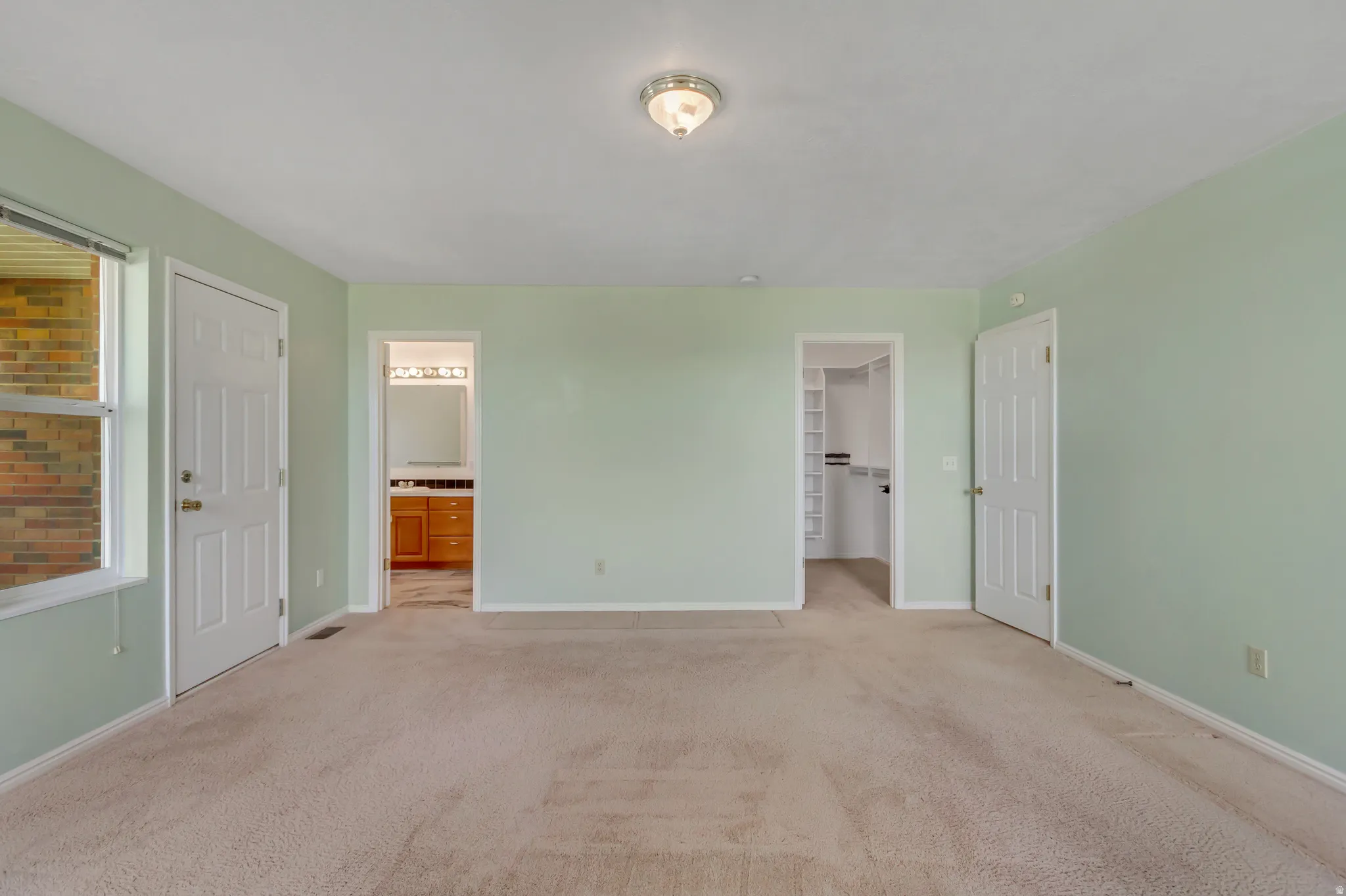 Carpeted room featuring light green walls, a window with brick exterior visibility, a ceiling-mounted light fixture, and two interior doors