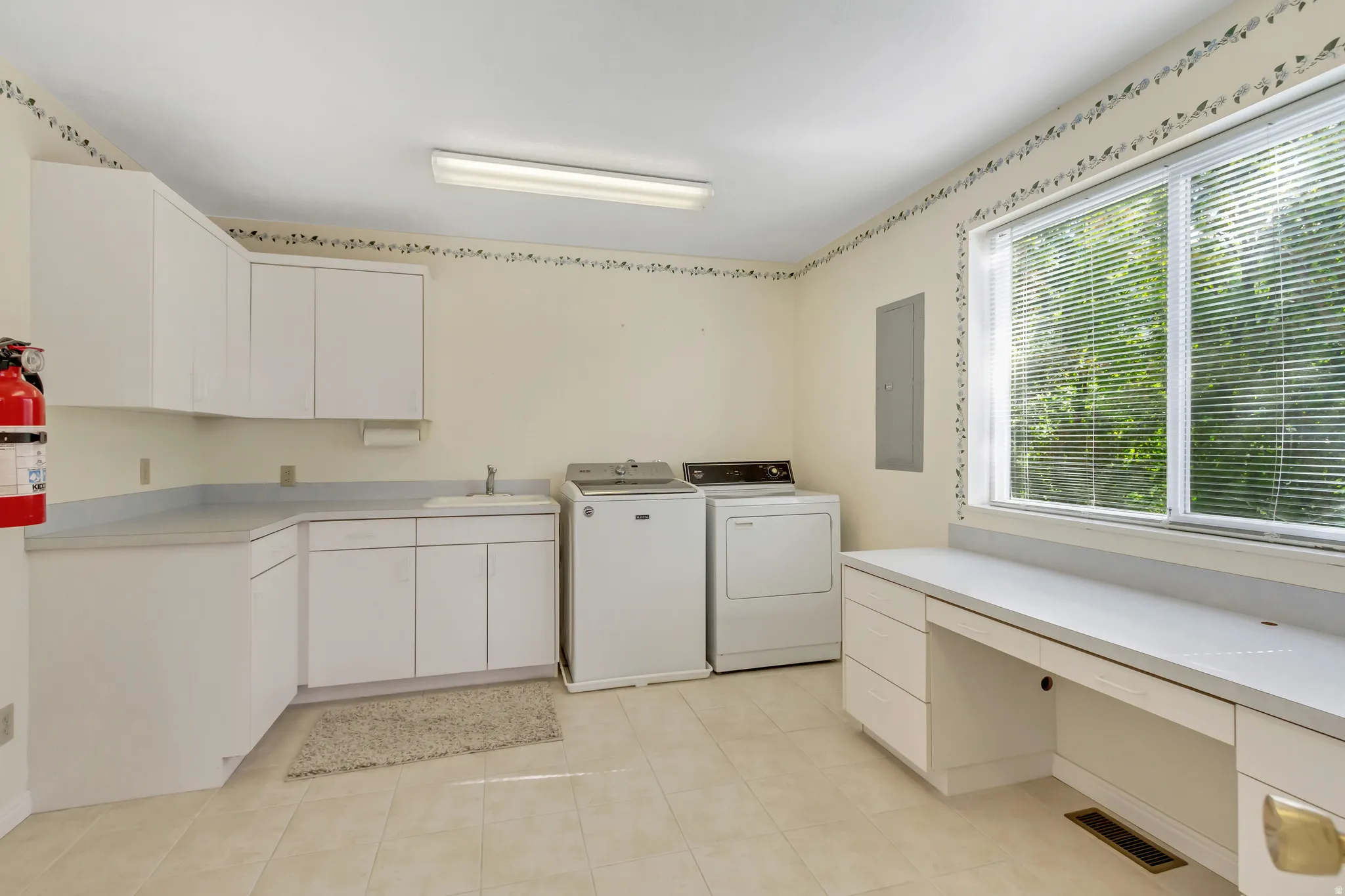 Utility room featuring white cabinetry, a sink, tile flooring, a large window, and a built-in desk