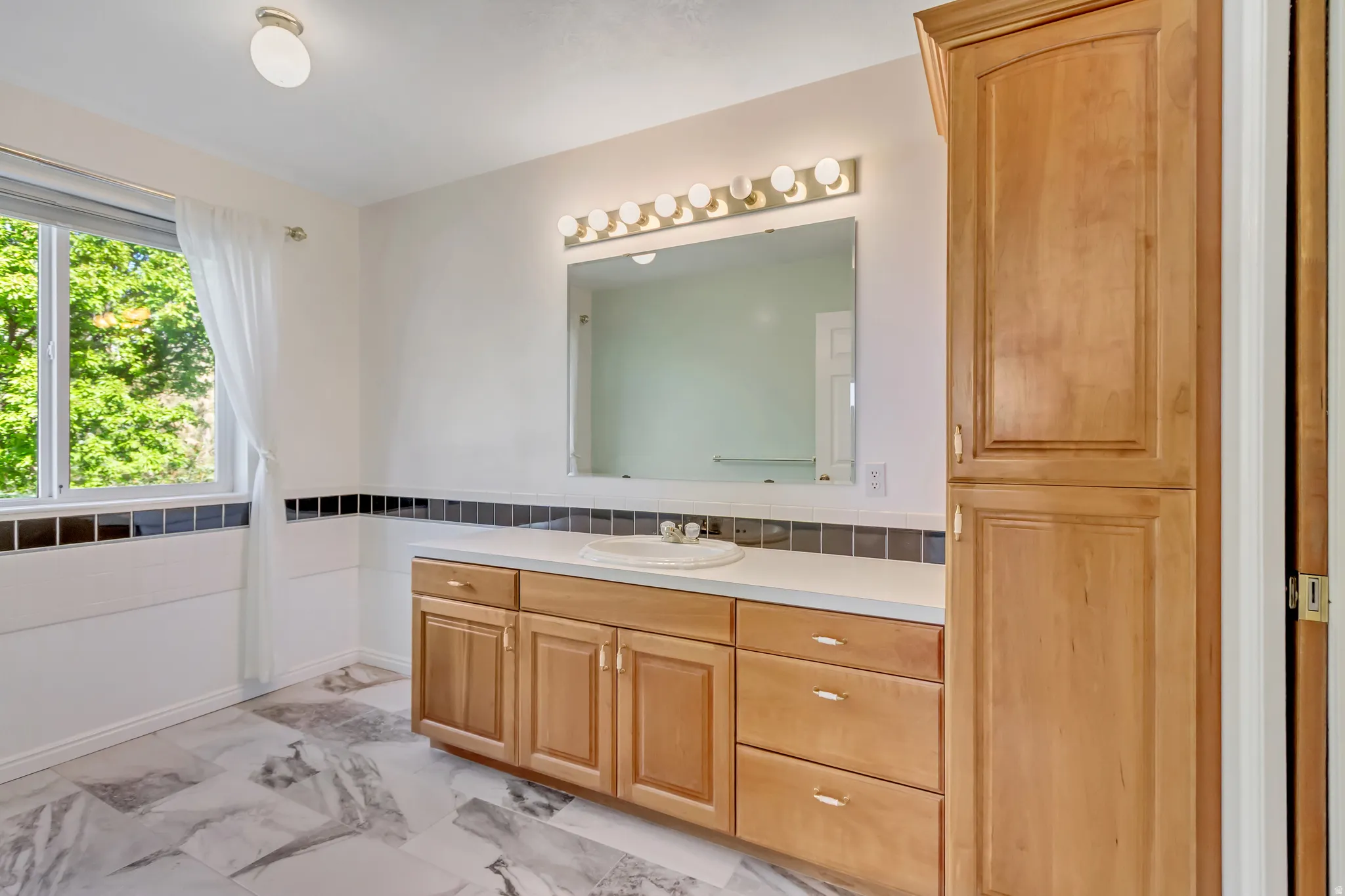 Bathroom featuring a single vanity with light wood cabinetry, a built-in storage cabinet, and a large mirror with overhead lighting