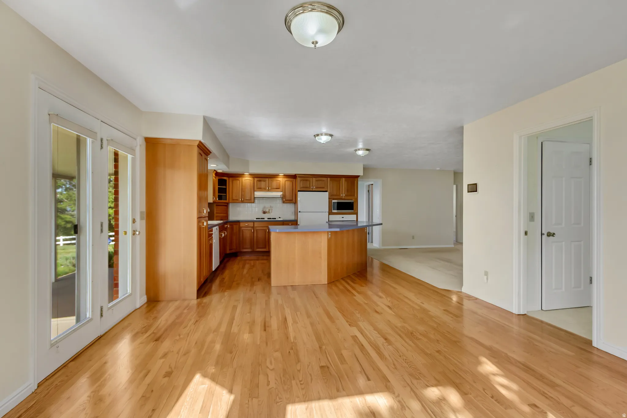Open-concept living space featuring wood-finish flooring, a kitchen with wood cabinetry and a central island, and double glass-panel doors