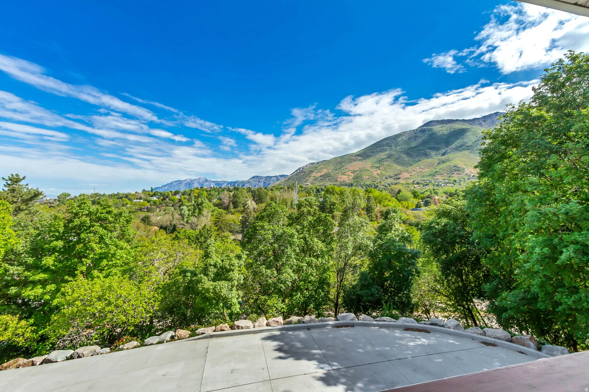 Paved outdoor terrace with a natural stone border and expansive mountain and tree canopy scenery
