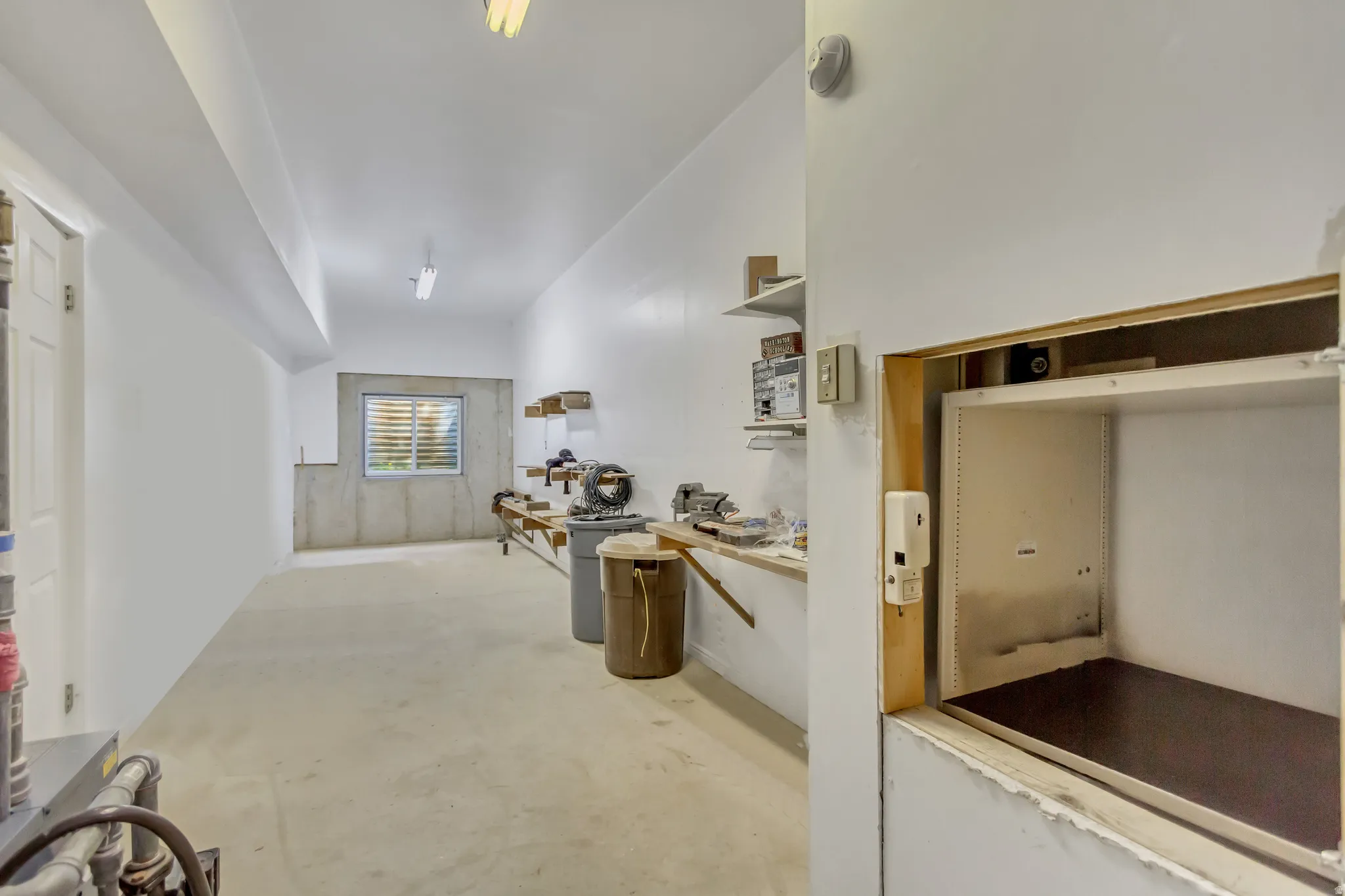 Spacious utility room featuring a built-in dumbwaiter, concrete flooring, and an integrated window