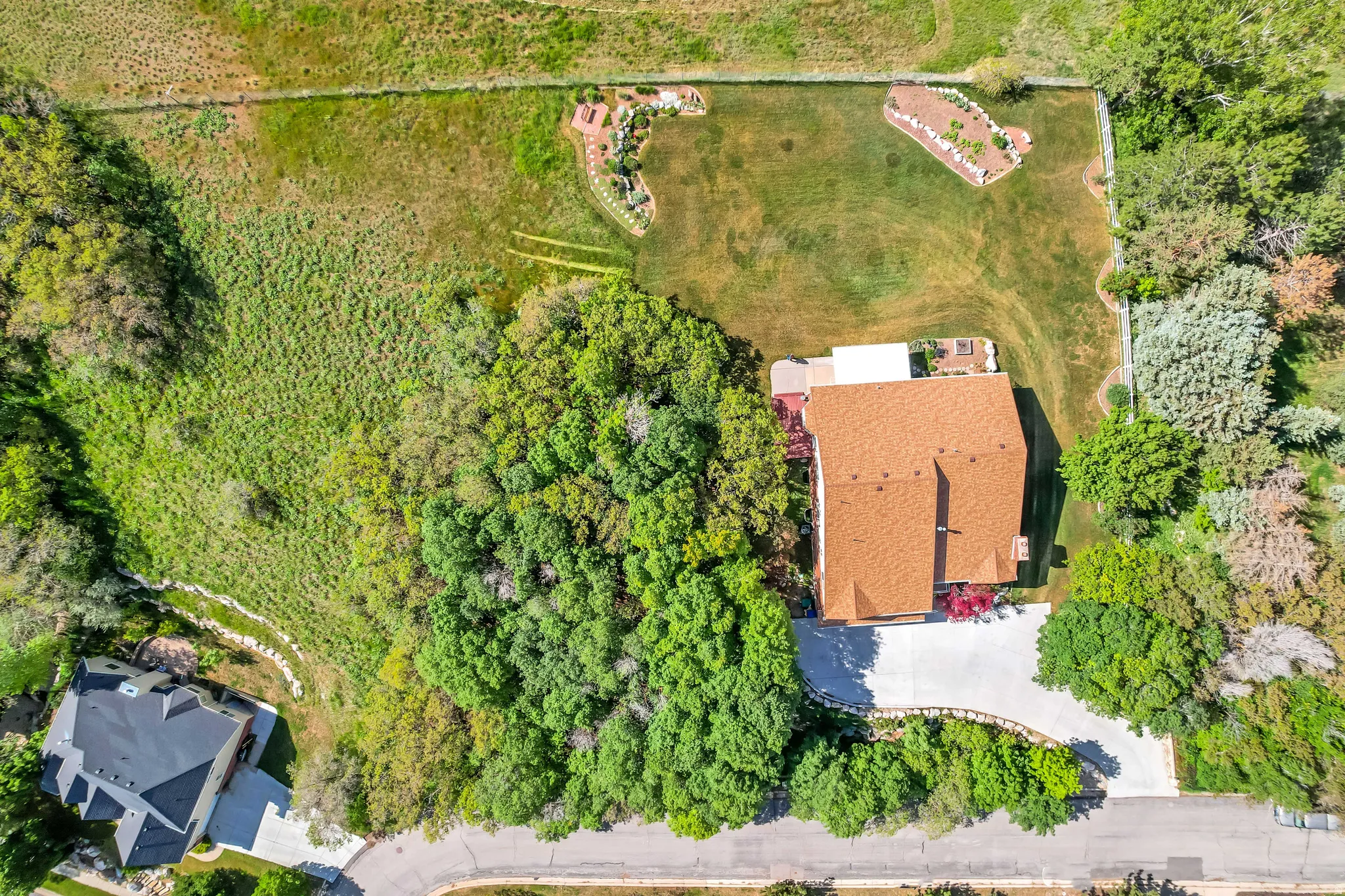 Expansive property featuring a residence with a brown shingle roof, a paved driveway, and a large, fenced green space