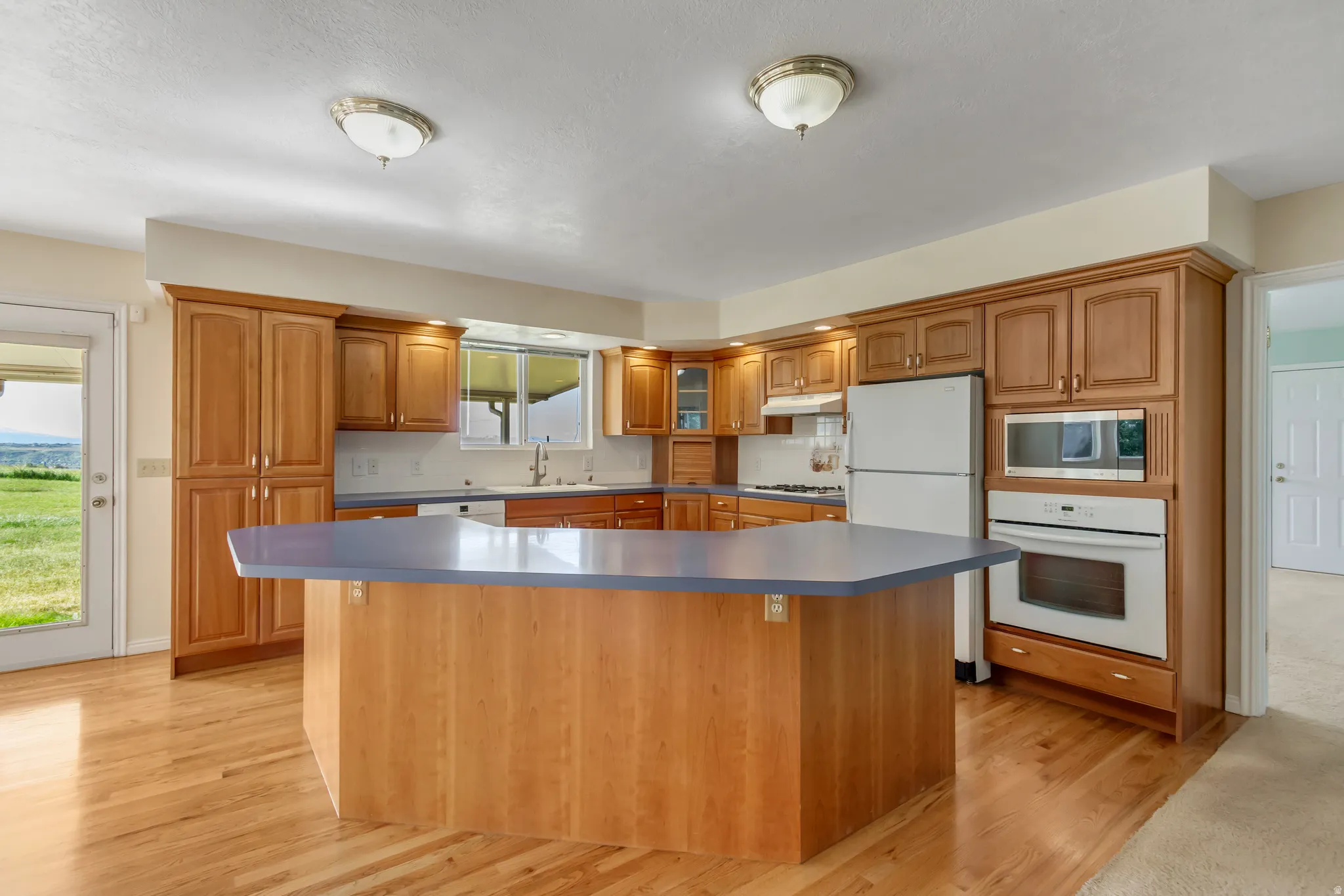 Kitchen featuring a hexagonal island with a solid surface countertop, wood cabinetry, a white appliance suite, and wood-finish flooring