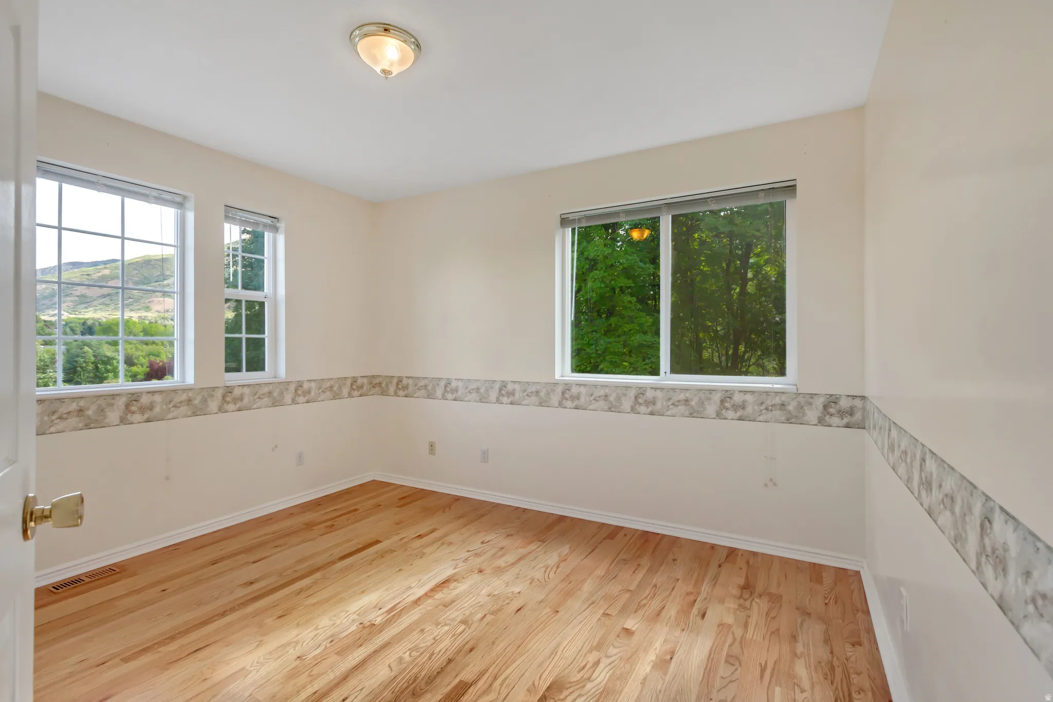 Room featuring natural wood flooring, multiple windows, and a flush-mount ceiling light