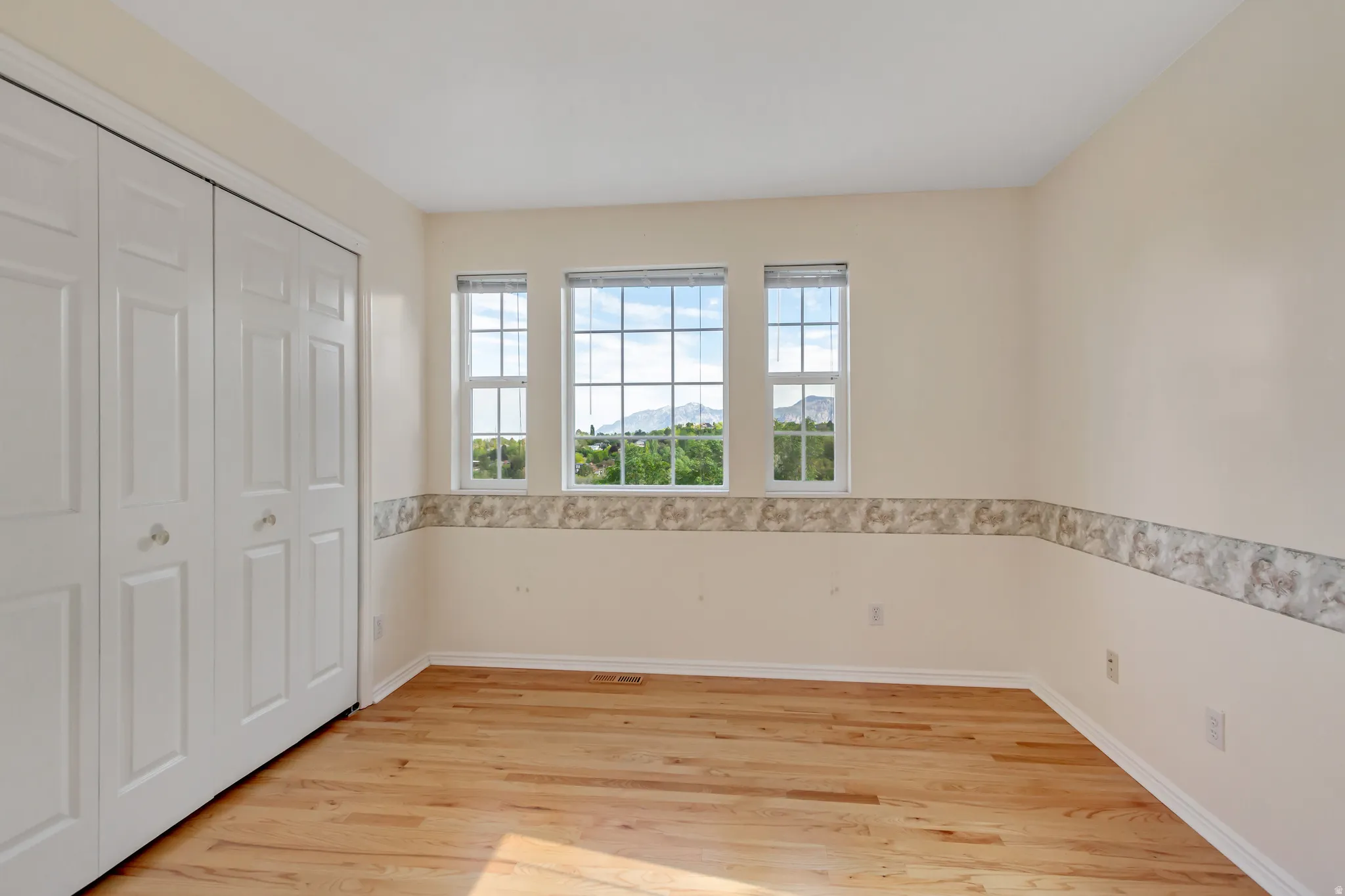 Room featuring a trio of windows, wood-finish flooring, and white trim