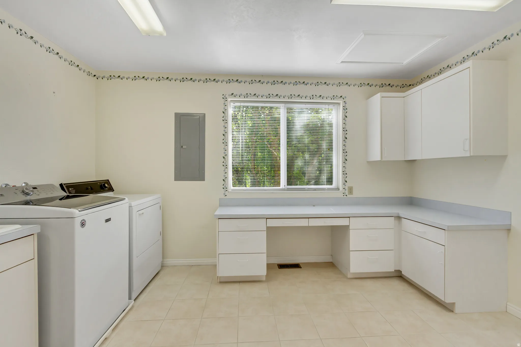 Spacious utility room featuring a large window, extensive counter space, ample cabinetry, and tile flooring