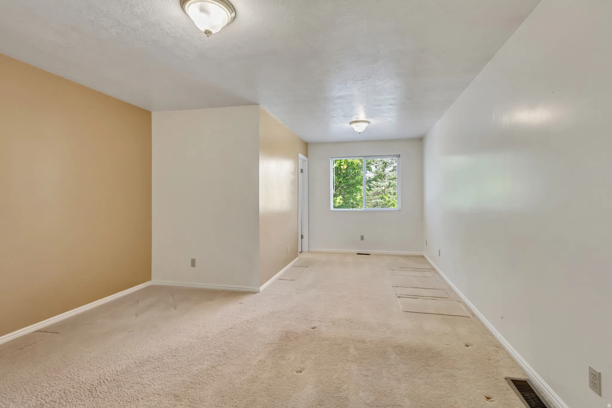 Spacious room featuring neutral carpet flooring, a large window with natural light, and two overhead flush-mount light fixtures