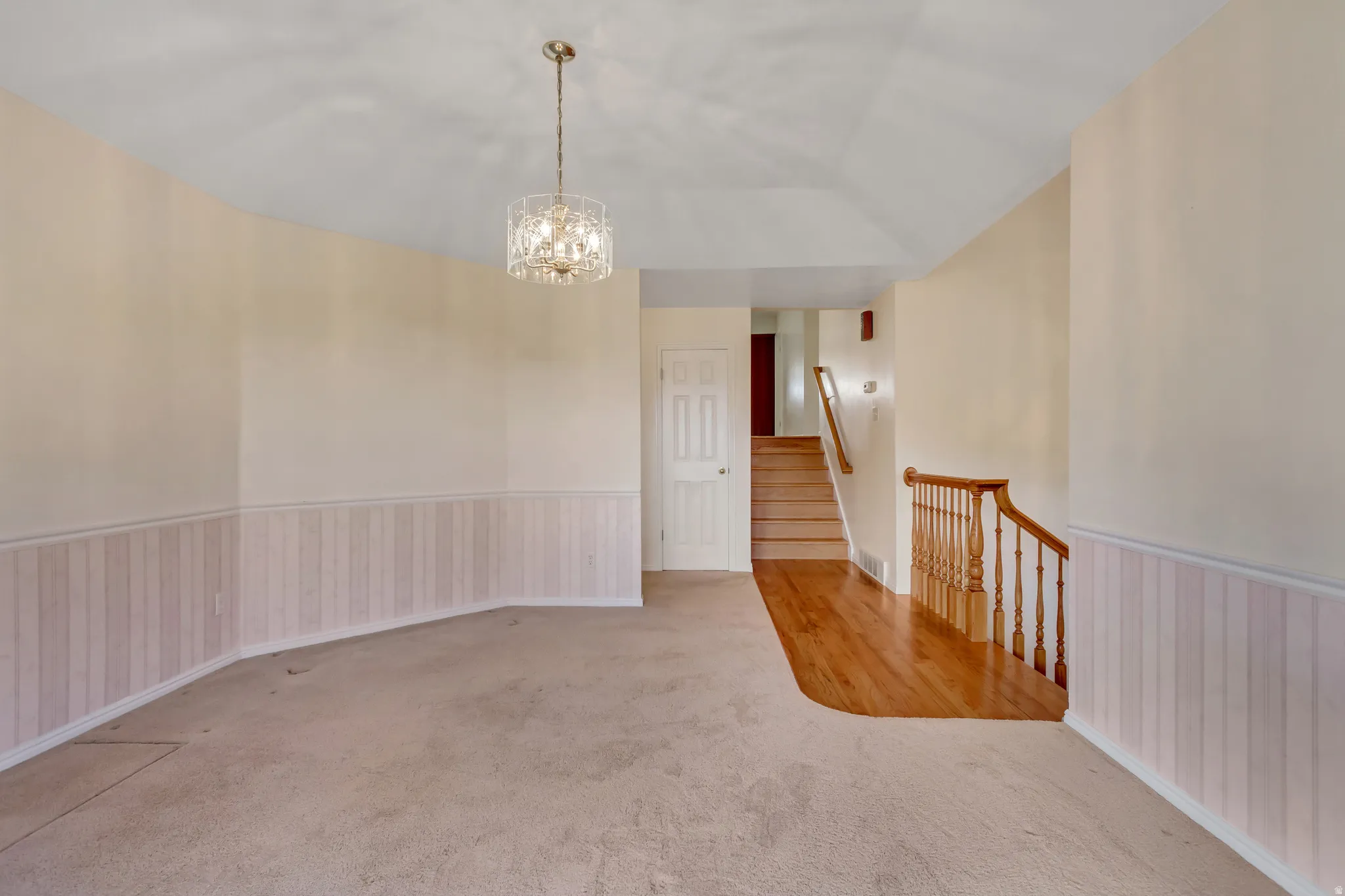 Entryway featuring a crystal chandelier, wood-finish flooring, staircase with wood banister, and wainscoting details