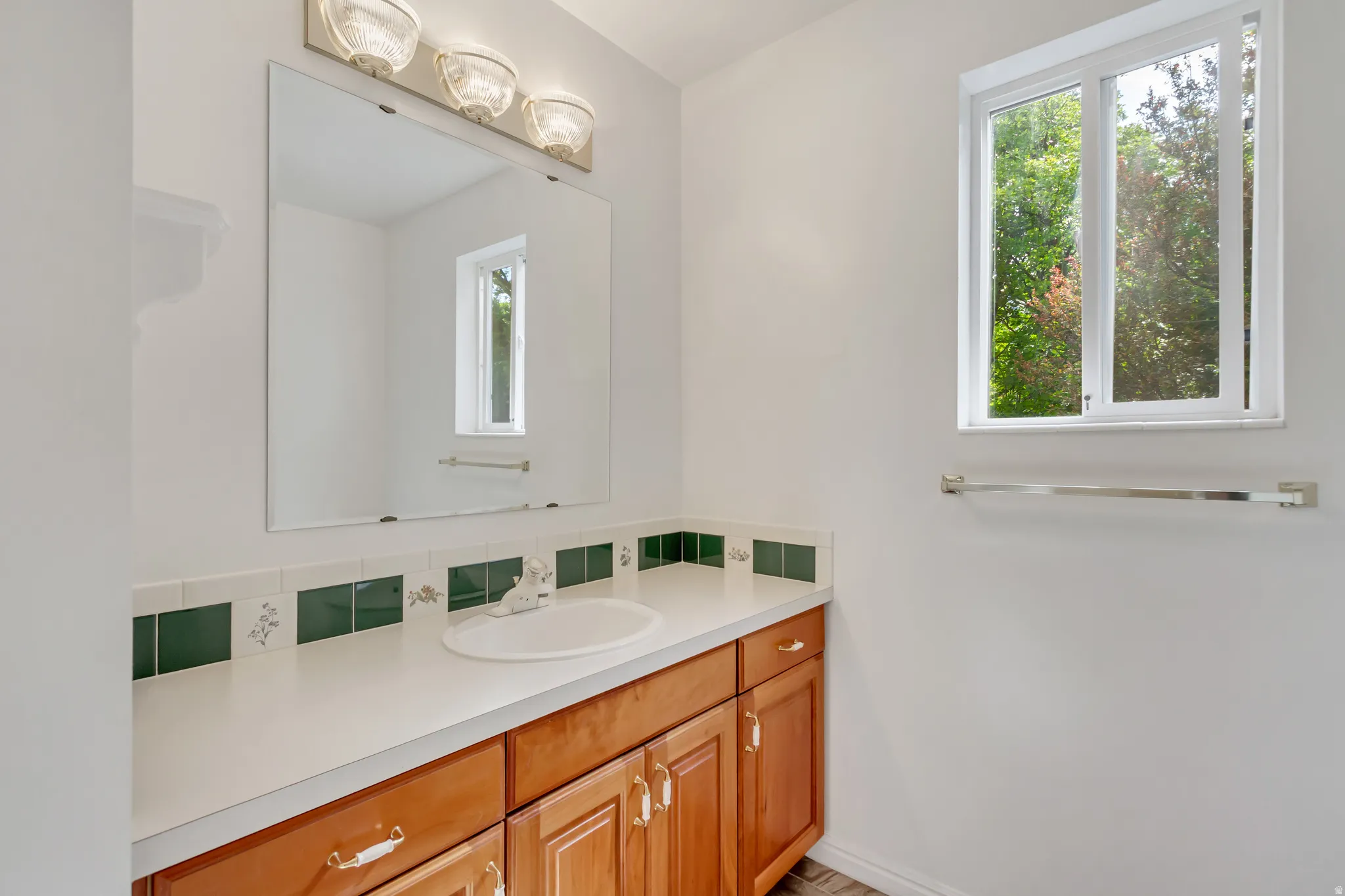 Bathroom vanity featuring a white countertop with an integrated sink, wood-finish cabinetry, and a full-width mirror