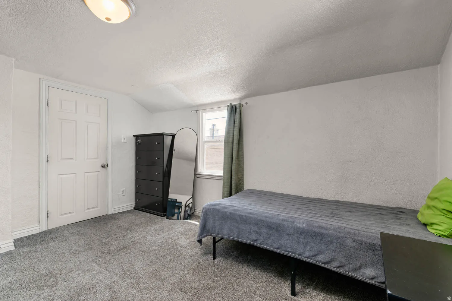 Carpeted room featuring a window with natural light, a white paneled door, and a textured ceiling