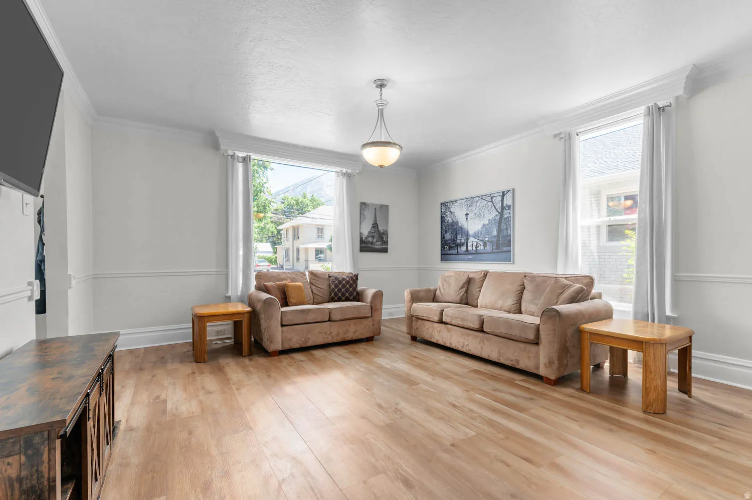 Spacious living area featuring light wood-finish flooring, white walls with wainscoting, and crown molding