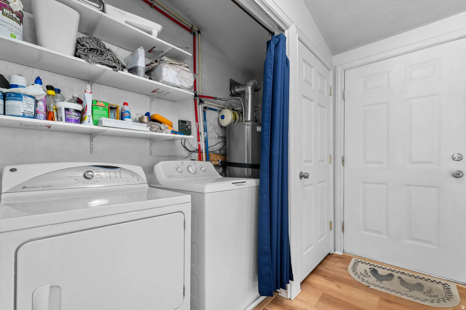 Dedicated laundry area featuring white shelving, a water heater, and wood-finish flooring