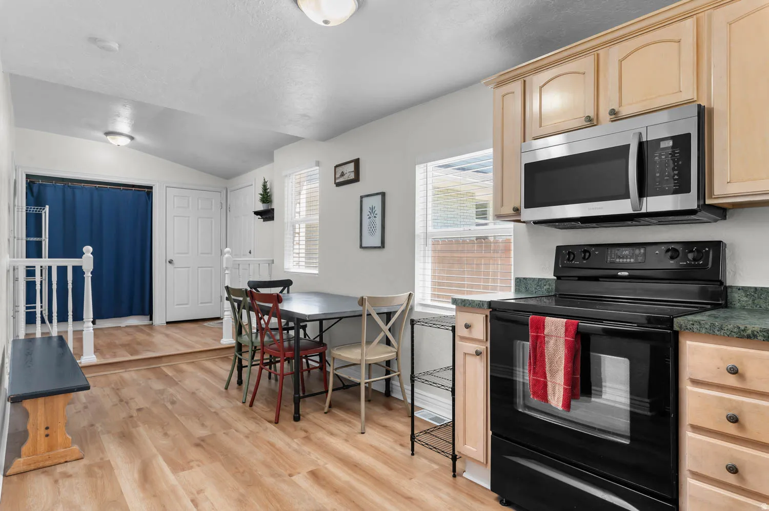 Open-concept kitchen and dining area featuring wood-finish flooring, light-toned cabinetry, stainless steel microwave, and black electric range