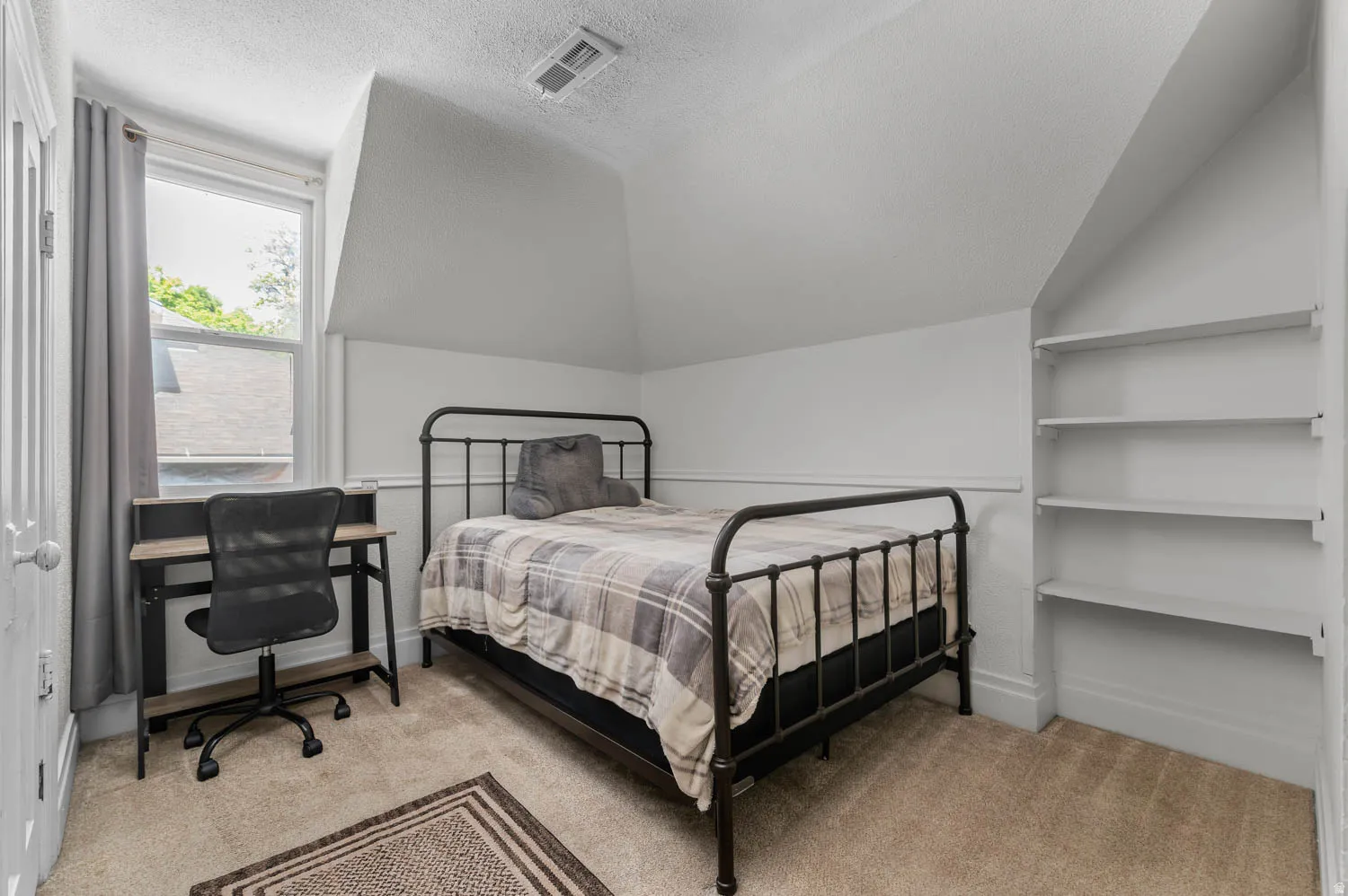 Carpeted room featuring a single window, built-in shelving, white trim, and sloped ceilings