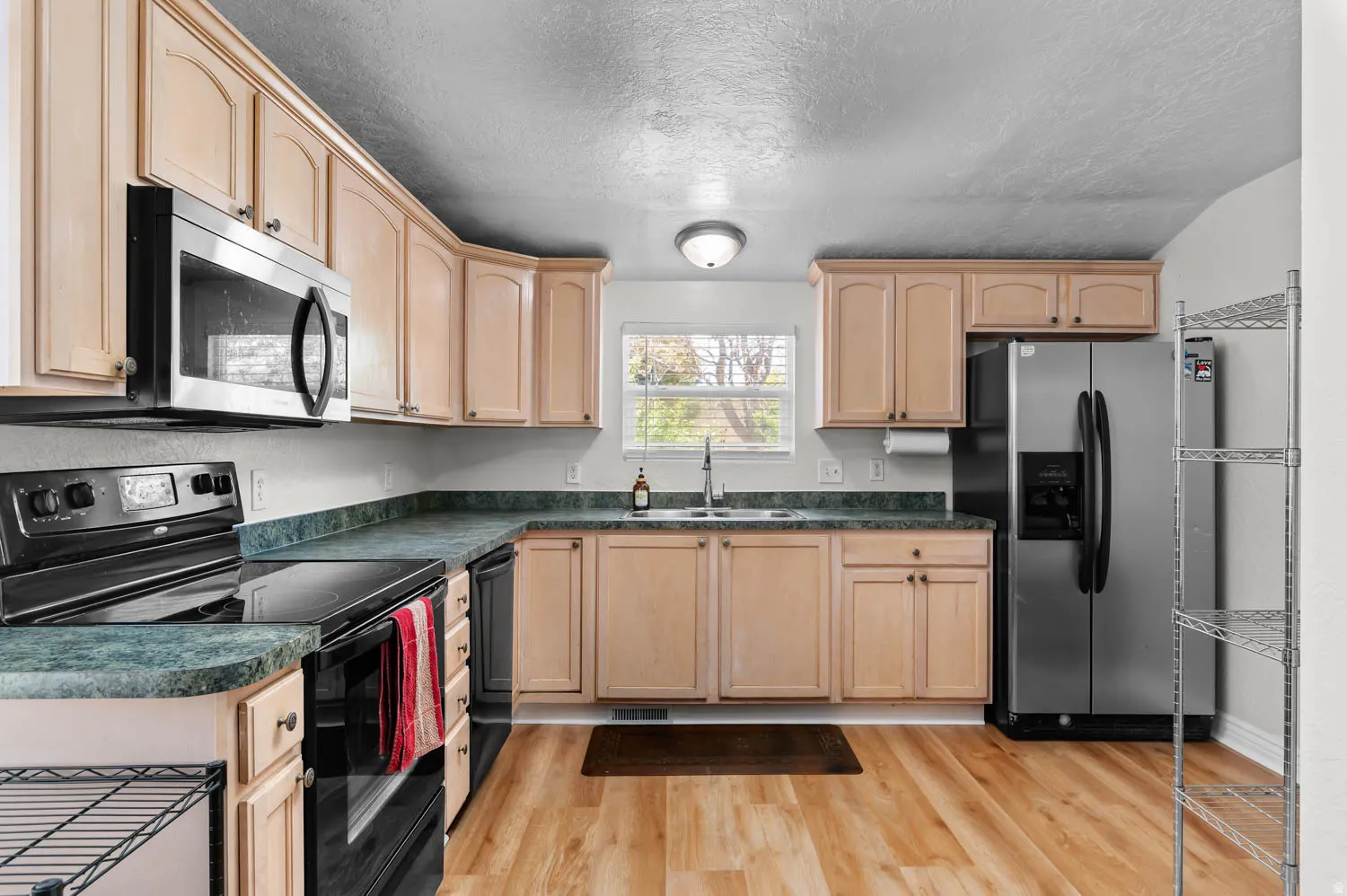 Kitchen featuring wood-finish flooring, light wood cabinetry, green countertops, and stainless steel appliances